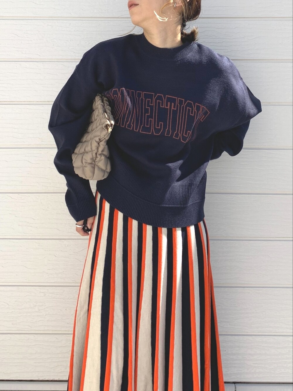 オレンジ系のスカート、ブルー系のニット/セーター、ベージュ系のショルダーバッグを着用したレディースの秋コーディネートの3枚目の写真