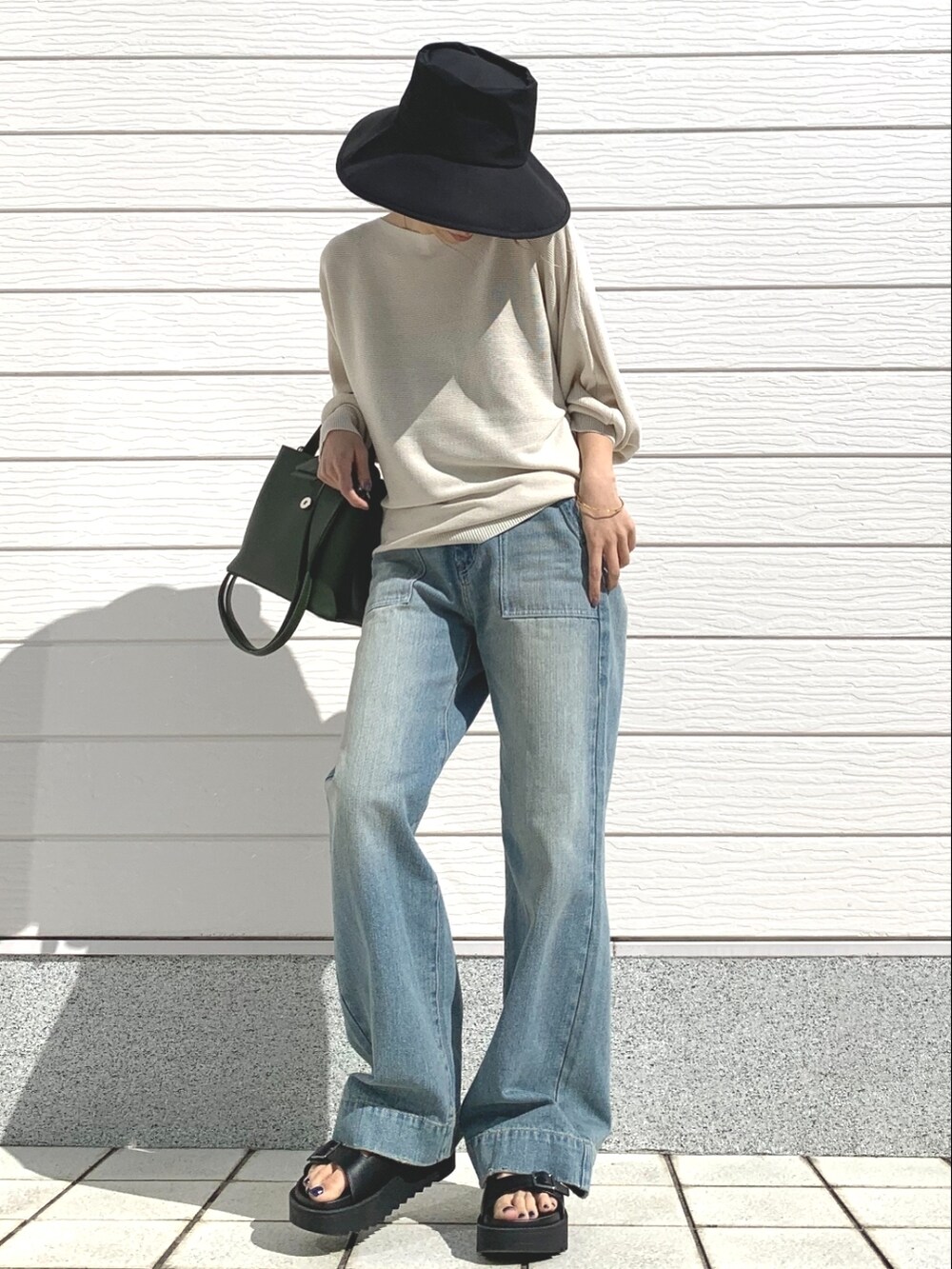 ブルー系のデニムパンツ、グリーン系のハンドバッグ、ブラック系のサンダルを着用したレディースの春コーディネートの2枚目の写真