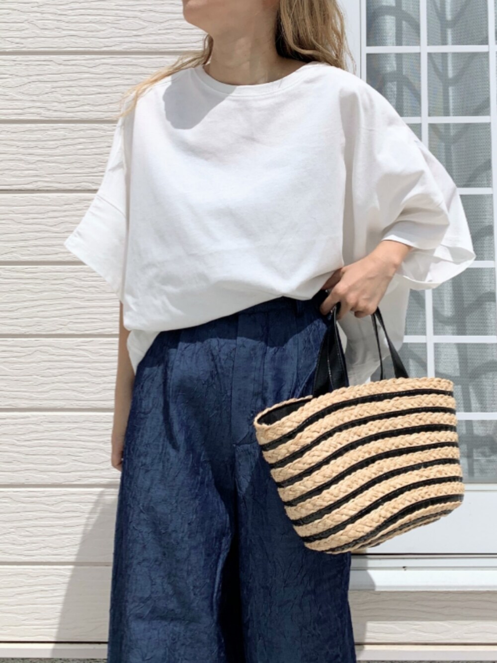 ホワイト系のTシャツ/カットソー、ブラック系のかごバッグ、ブルー系のデニムパンツを着用したレディースの春コーディネートの4枚目の写真