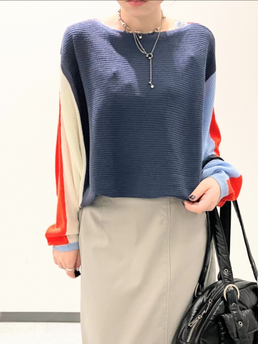 オレンジ系のニット/セーター、グレー系のスカート、ブラック系のボストンバッグを着用したレディースの秋コーディネートの5枚目の写真