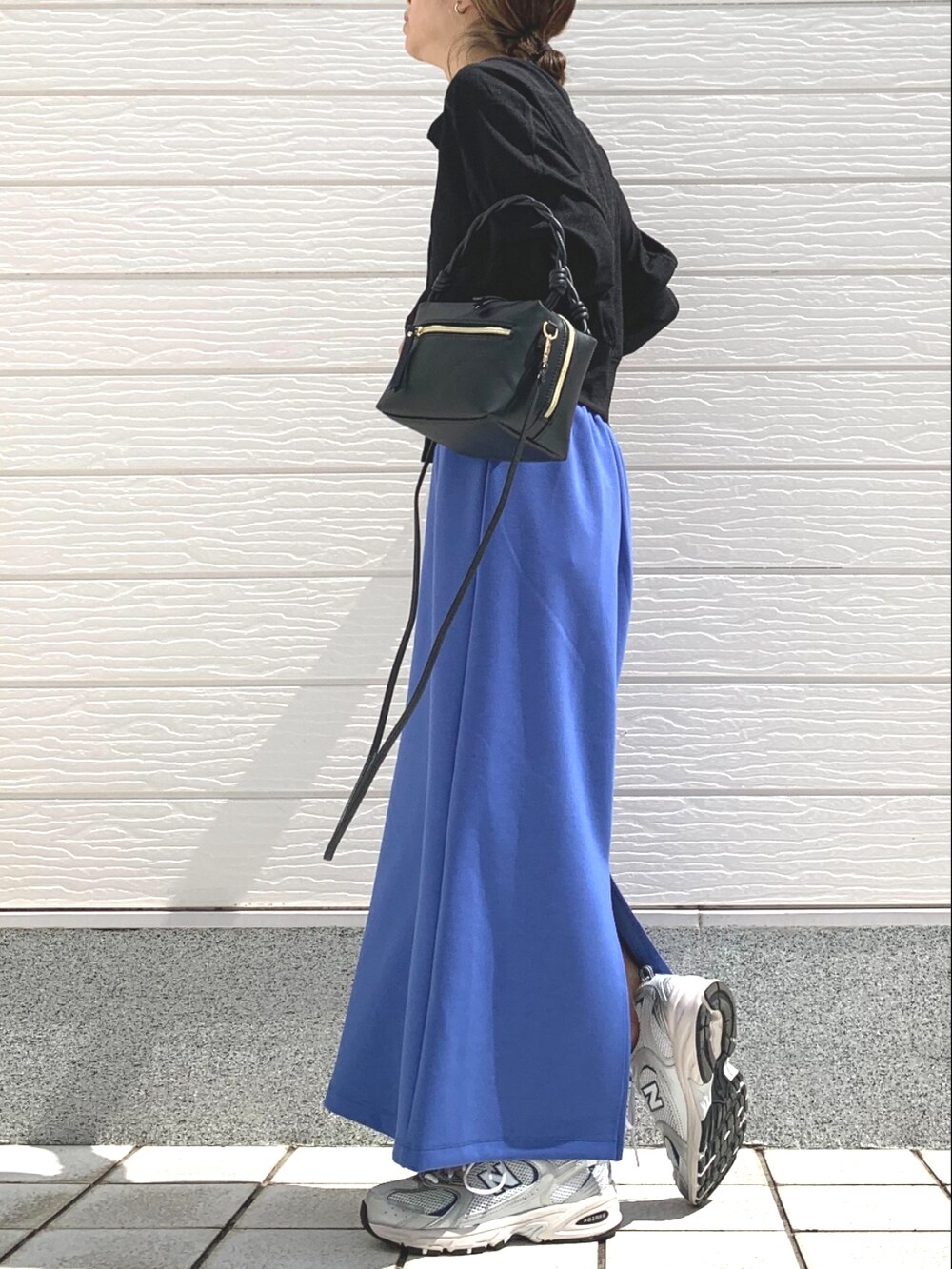 シルバー系のスニーカー、ブルー系のスカート、ブラック系のハンドバッグを着用したレディースの春コーディネートの2枚目の写真