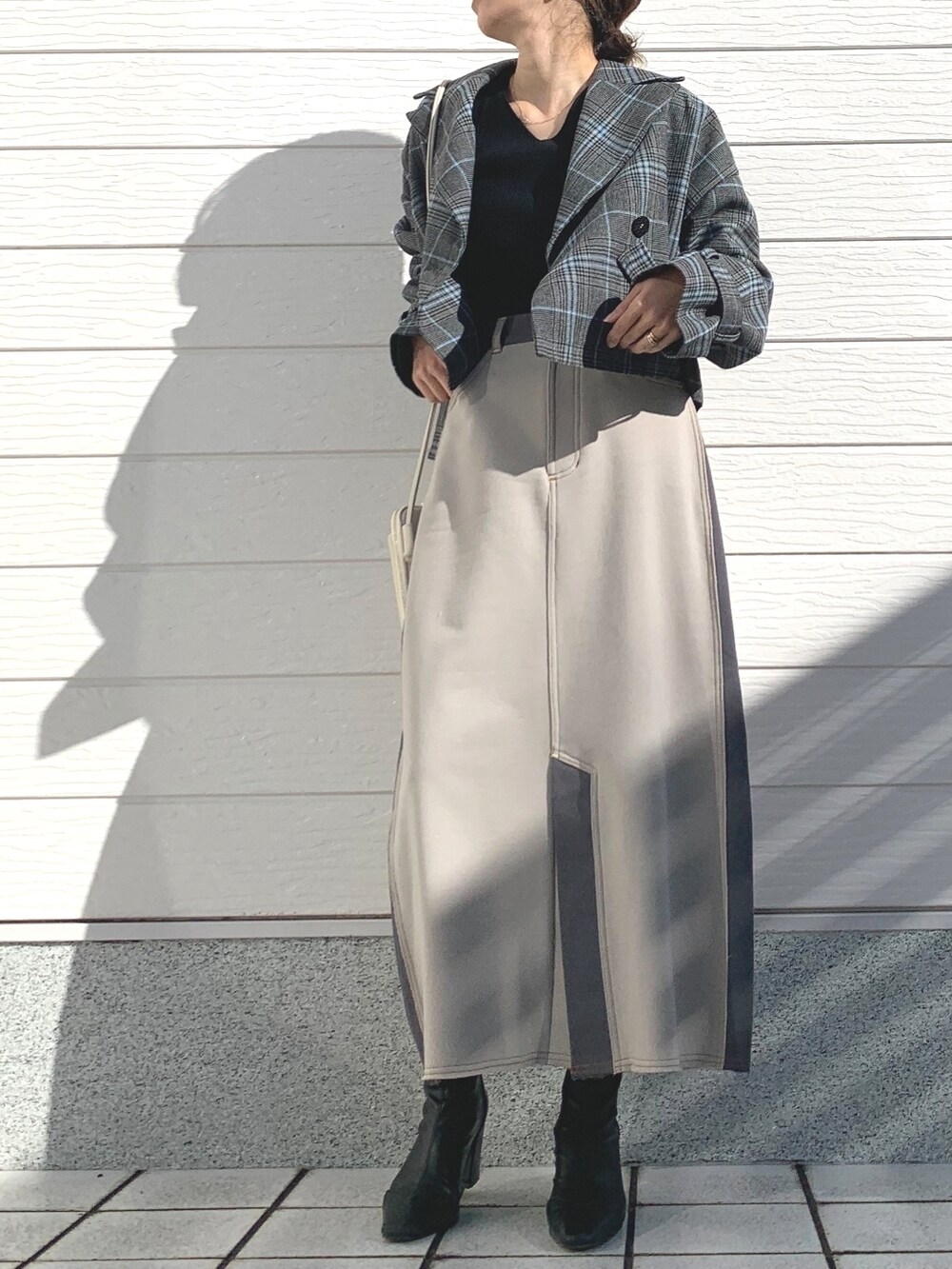グレー系のトレンチコート、ブラック系のニット/セーター、ホワイト系のスカートを着用したレディースの冬コーディネートの2枚目の写真