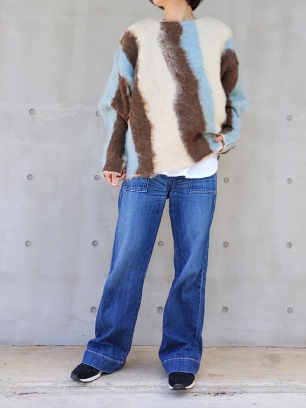 ブルー系のデニムパンツ、ブルー系のニット/セーター、ブラック系のスニーカーを着用したレディースの秋コーディネートの2枚目の写真