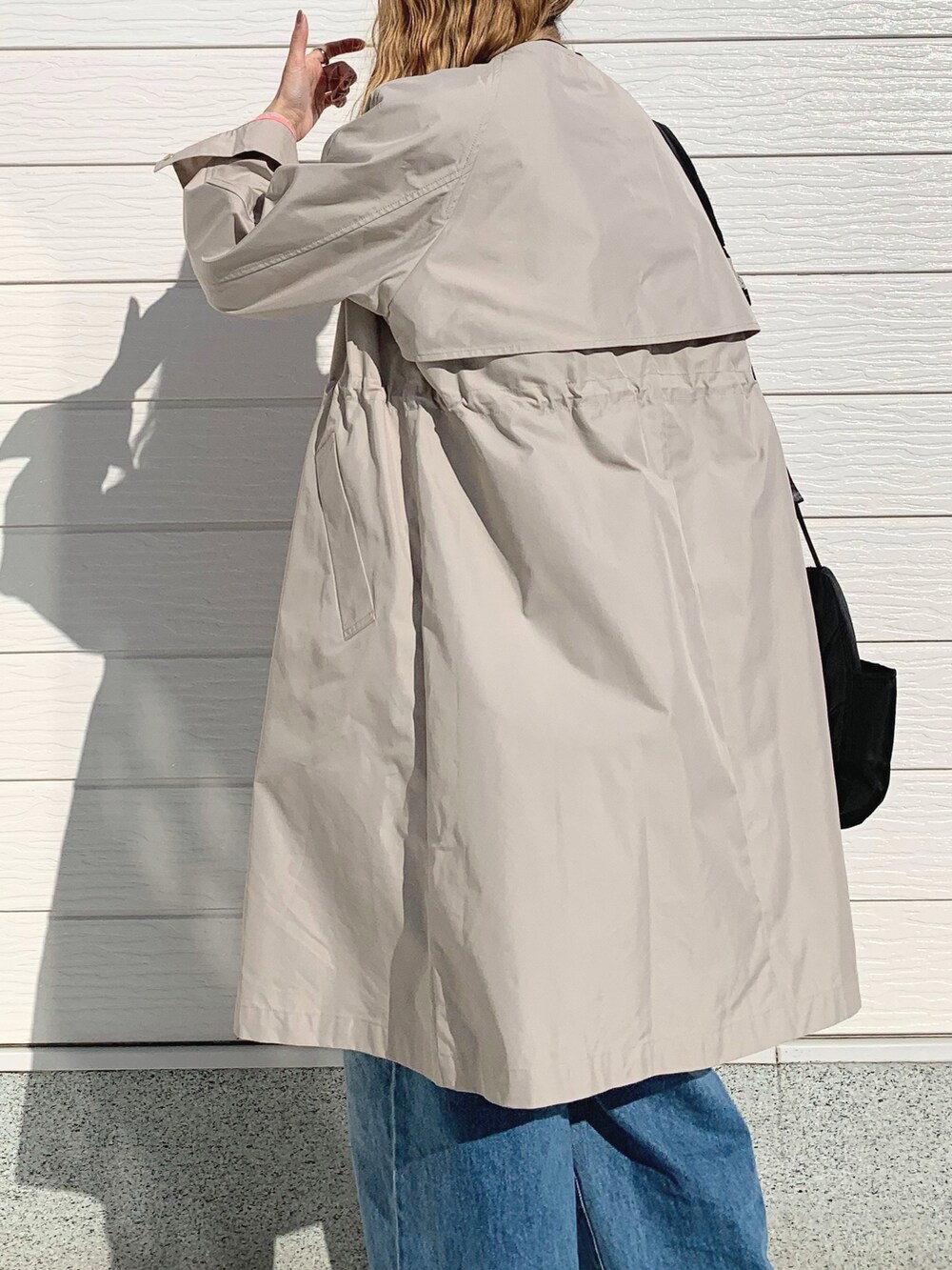 ブルー系のデニムパンツ、ブラック系のショルダーバッグ、ベージュ系のノーカラーコートを着用したレディースの春コーディネートの4枚目の写真