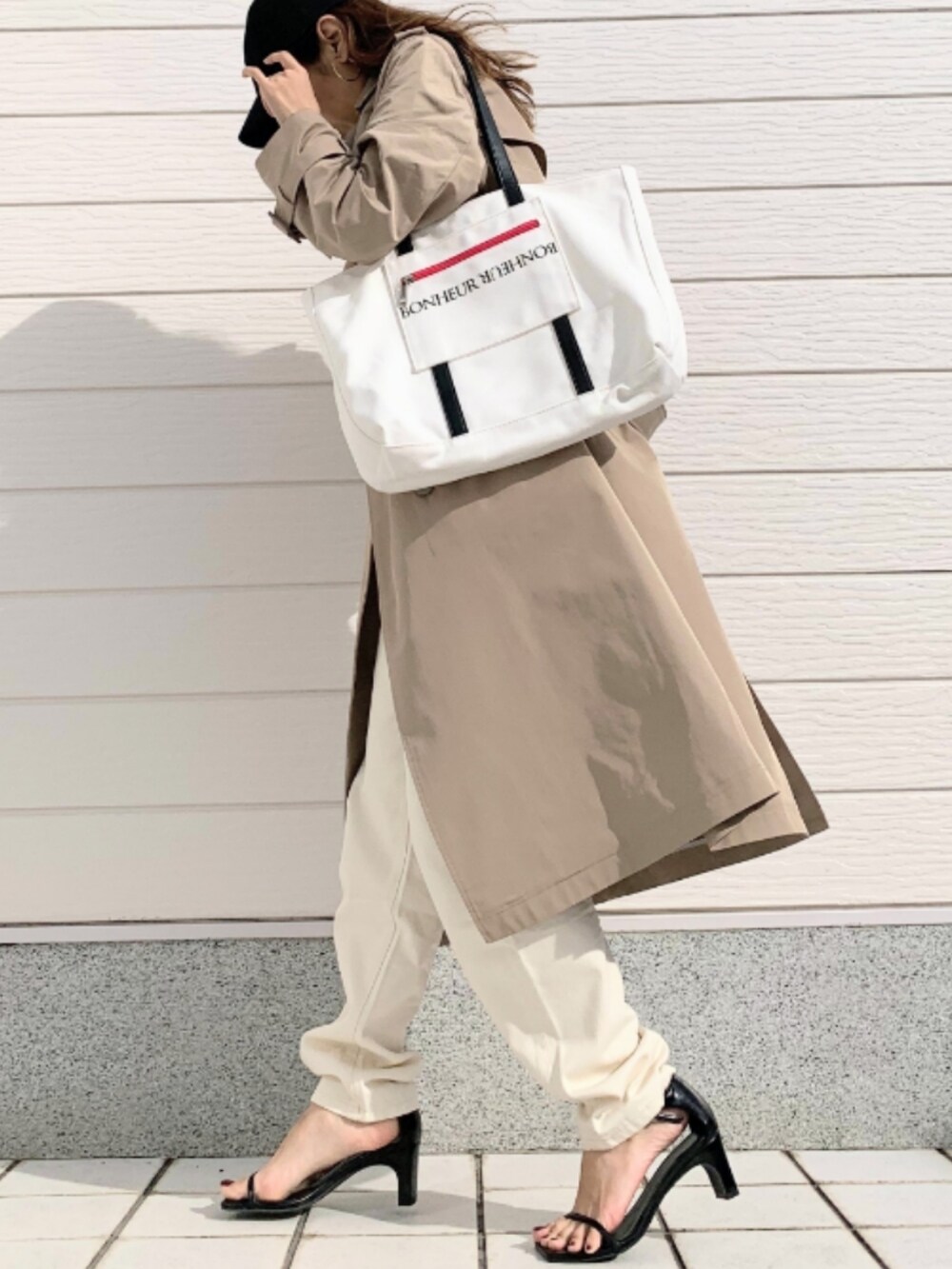 ホワイト系のトートバッグ、ベージュ系のトレンチコート、ブラック系のTシャツ/カットソーを着用したレディースの冬コーディネートの2枚目の写真