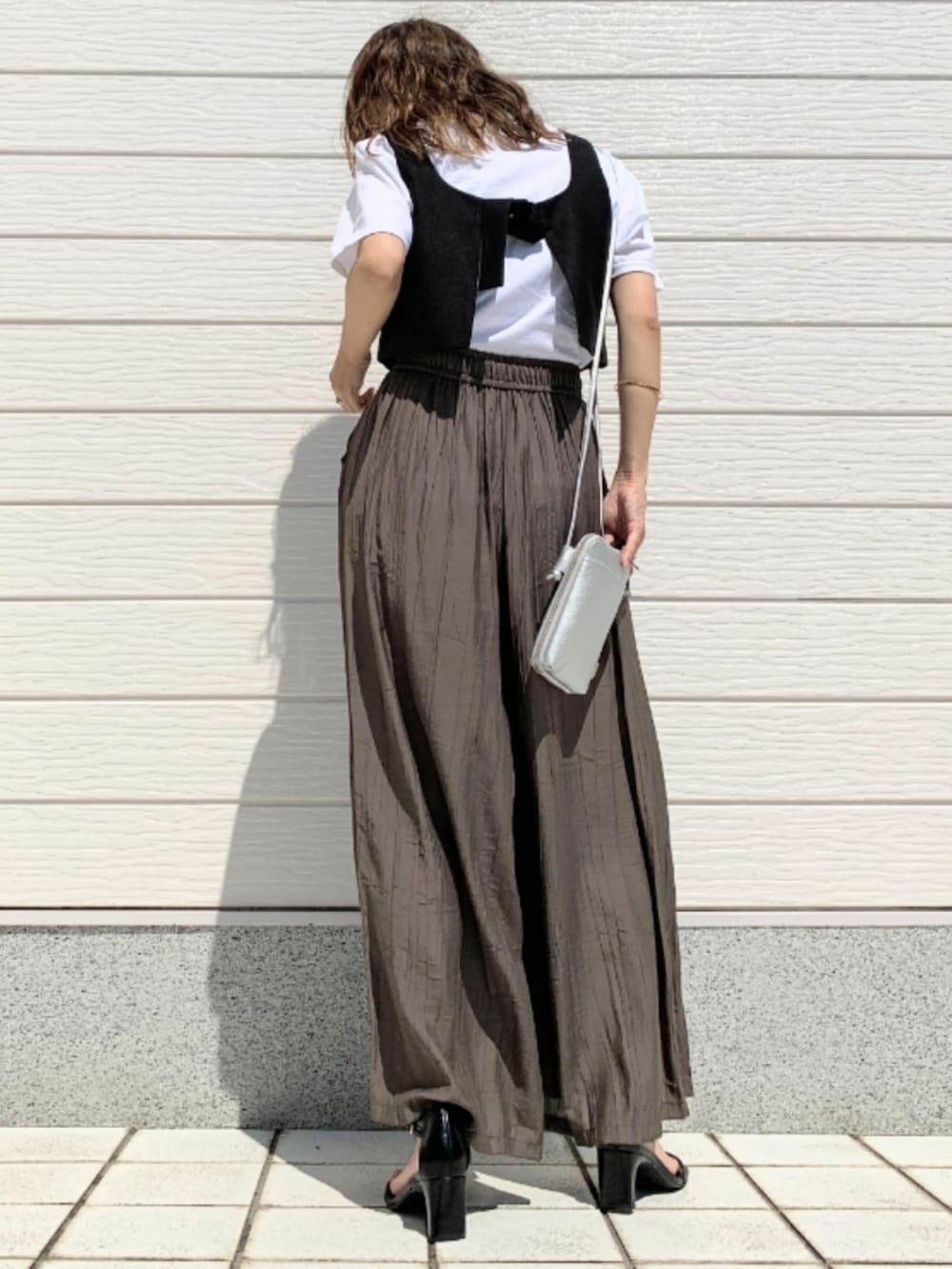 シルバー系のショルダーバッグ、ブラック系のベスト、ホワイト系のTシャツ/カットソーを着用したレディースの夏コーディネートの3枚目の写真
