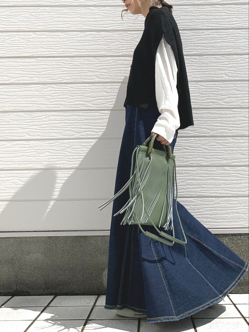 ブルー系のデニムスカート、ブラック系のスニーカー、ブラック系のベストを着用したレディースの秋コーディネートの2枚目の写真