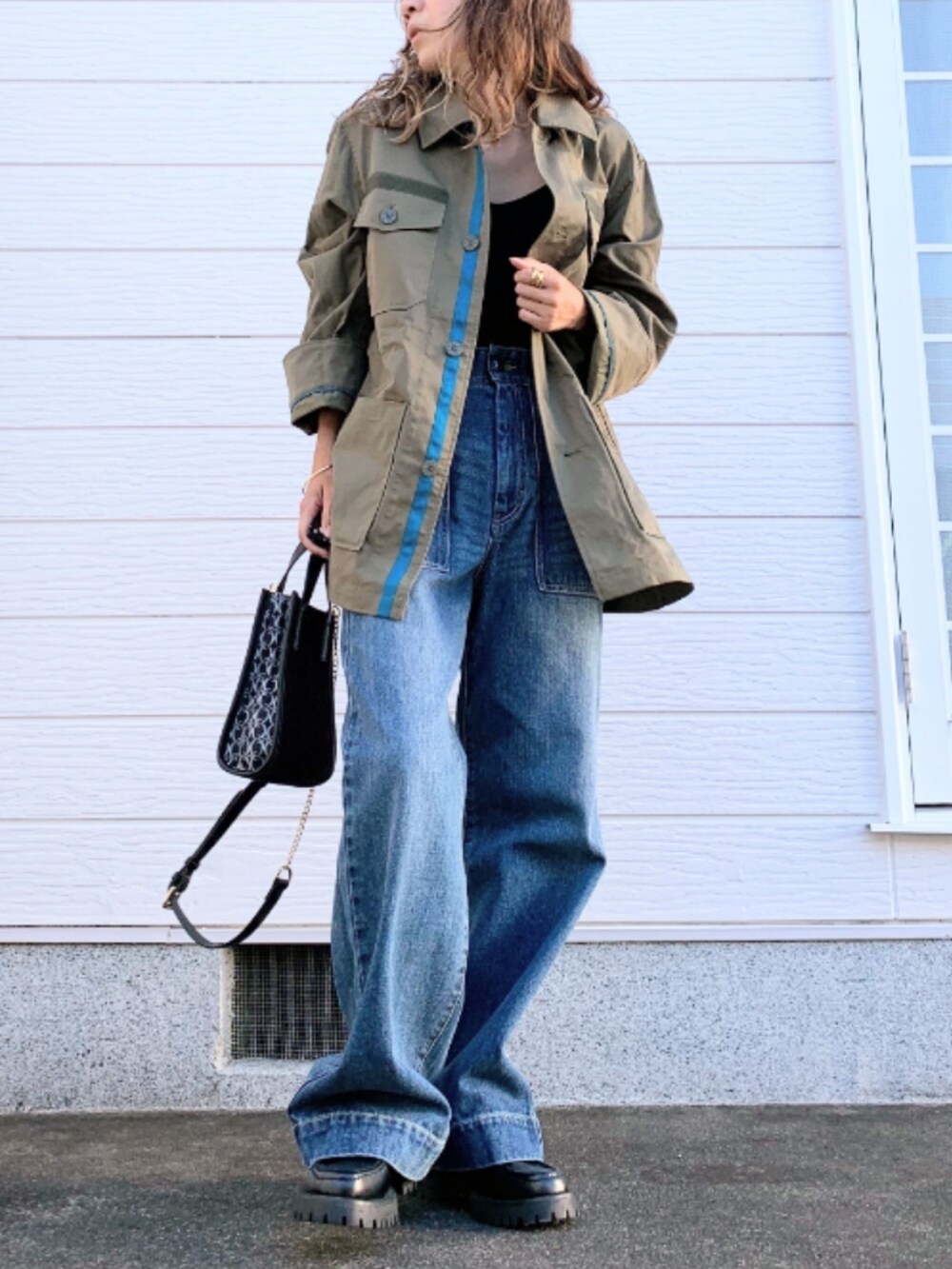 ブルー系のデニムパンツ、グリーン系のミリタリージャケット、ブラック系のショルダーバッグを着用したレディースの秋コーディネートの2枚目の写真