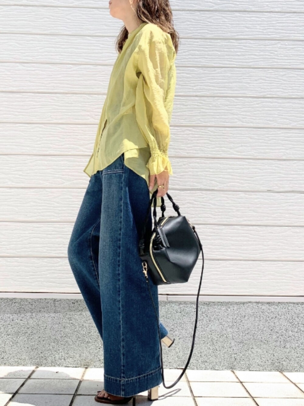 ブルー系のデニムパンツ、ブラウン系のサンダル、ブラック系のハンドバッグを着用したレディースの春コーディネートの2枚目の写真