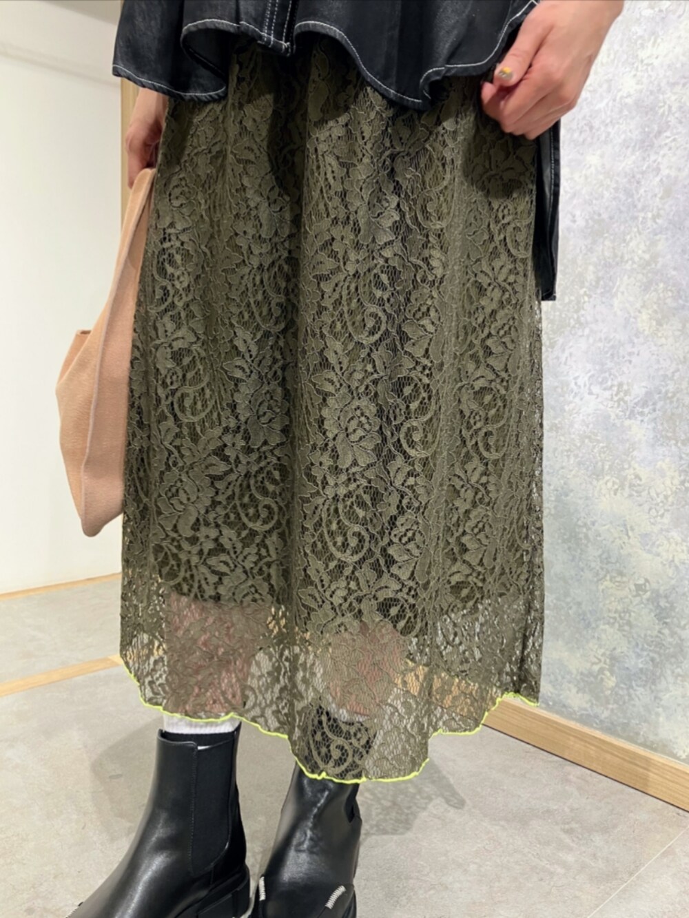 ブラック系のブーツ、グリーン系のスカート、ベージュ系のトートバッグを着用したレディースの秋コーディネートの4枚目の写真