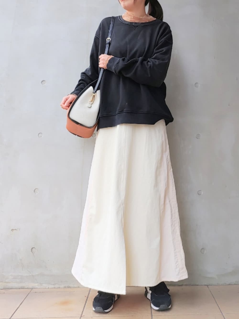 ブラック系のスウェット、ホワイト系のデニムスカート、ブラック系のスニーカーを着用したレディースの冬コーディネートの2枚目の写真