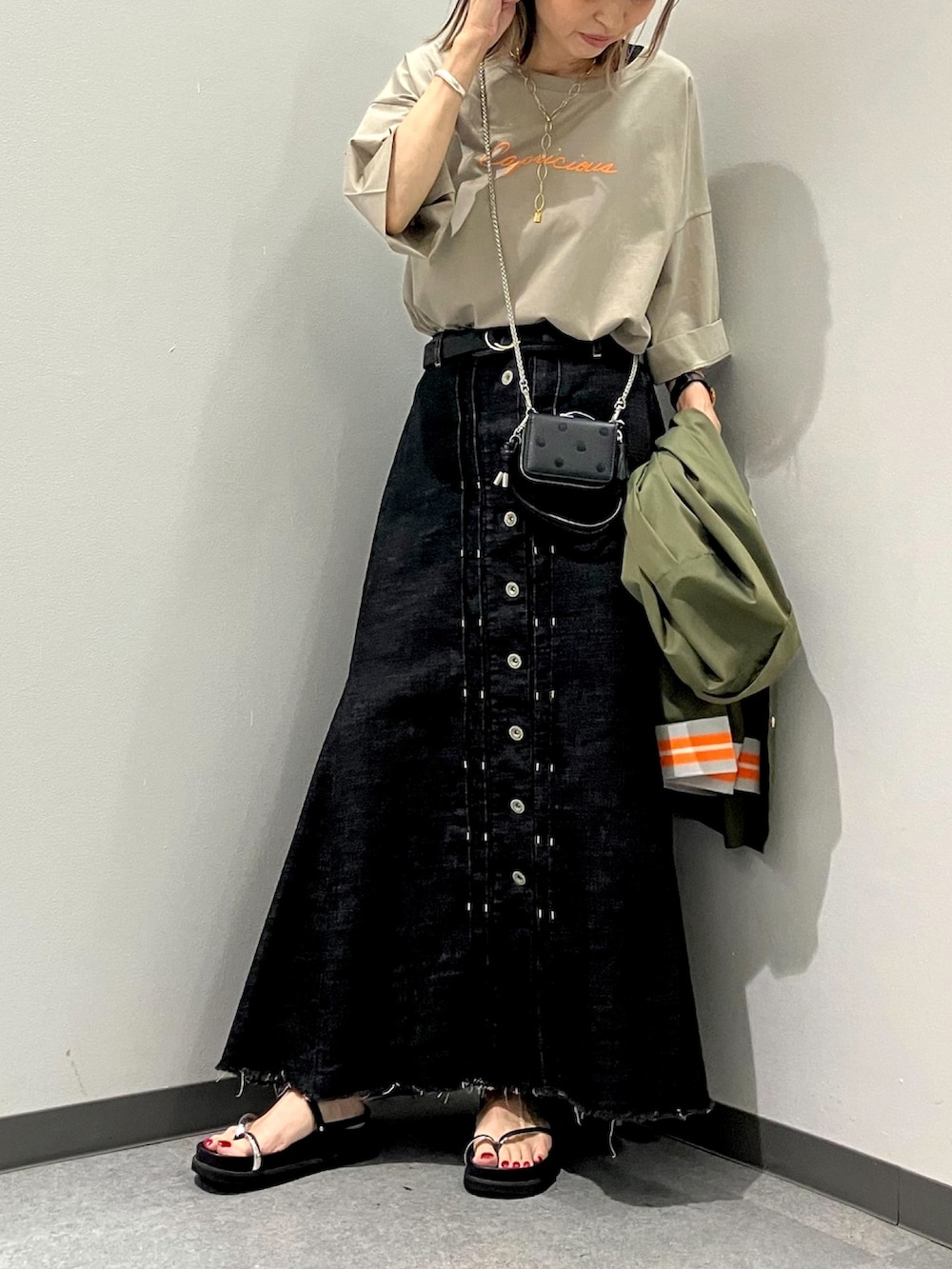 ブラック系のデニムスカート、ベージュ系のTシャツ/カットソー、ブラック系のサンダルを着用したレディースの夏コーディネートの2枚目の写真