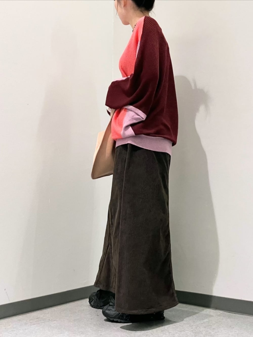 レッド系のニット/セーター、ブラウン系のスカート、ベージュ系のトートバッグを着用したレディースの秋コーディネートの3枚目の写真