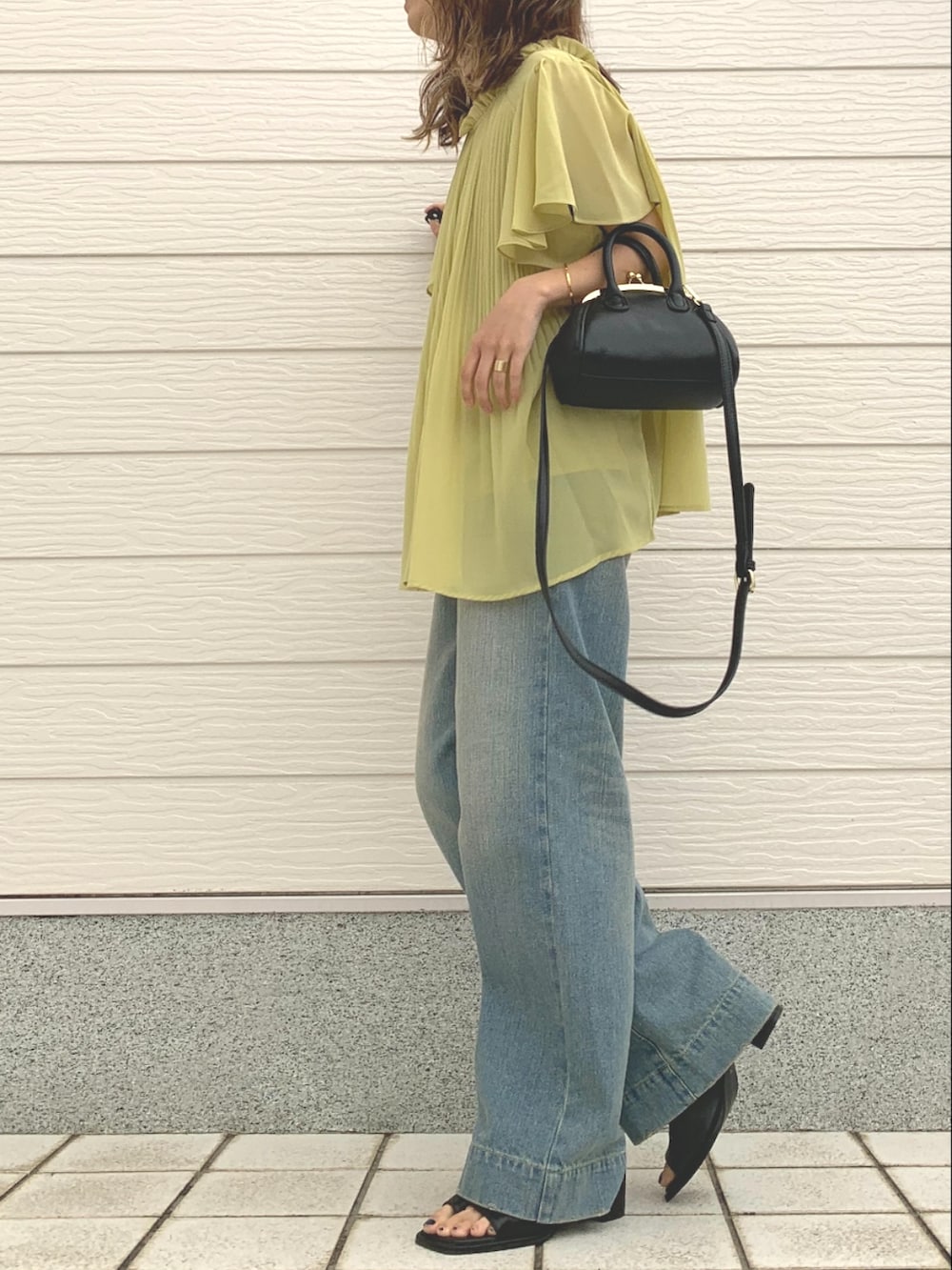 ブラック系のショルダーバッグ、ブルー系のデニムパンツ、ブラック系のサンダルを着用したレディースの春コーディネートの2枚目の写真