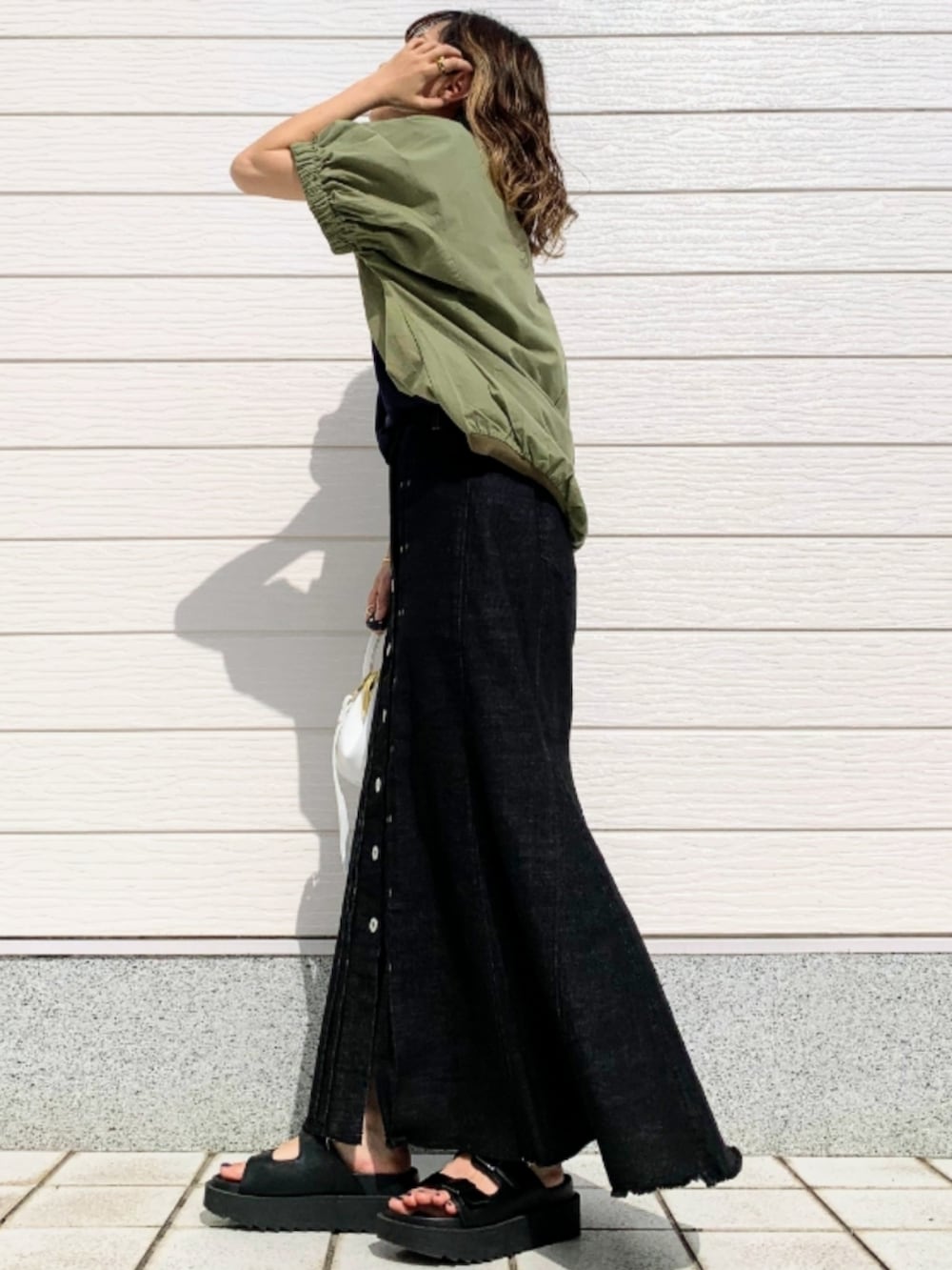 ブラック系のデニムスカート、ブラック系のサンダル、ホワイト系のショルダーバッグを着用したレディースの春コーディネートの3枚目の写真