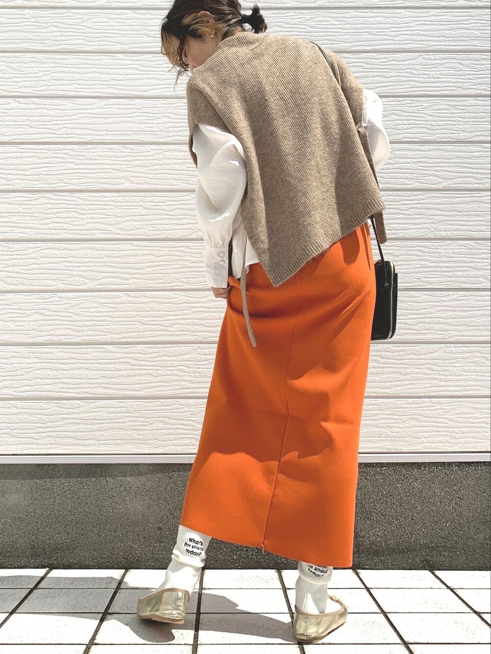ブラック系のショルダーバッグ、オレンジ系のスカート、イエロー系のベストを着用したレディースの秋コーディネートの2枚目の写真