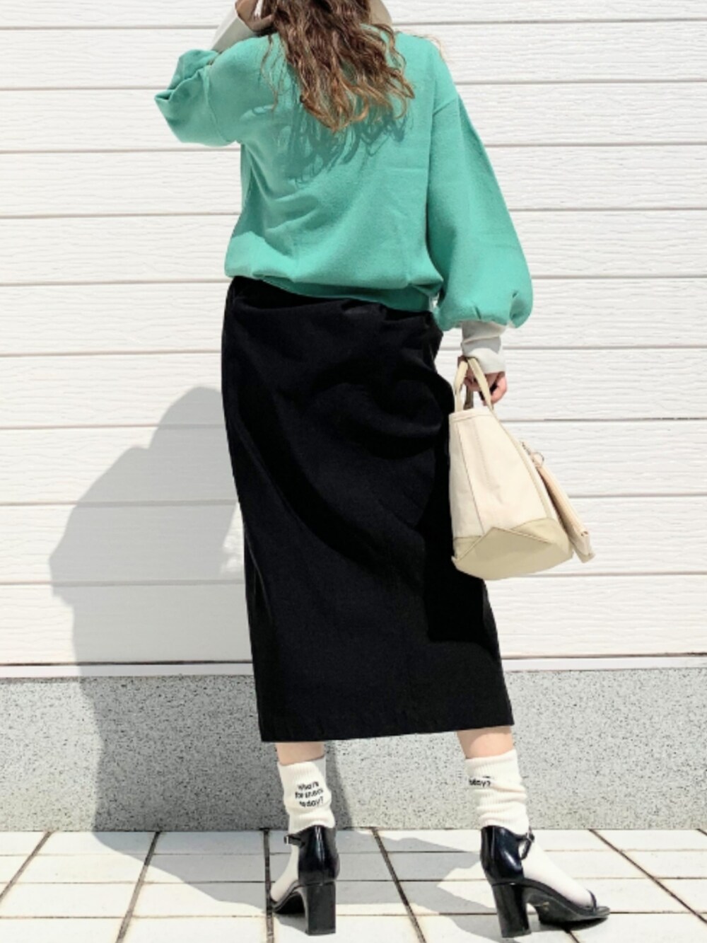 ベージュ系のトートバッグ、ブラック系のスカート、グリーン系のニット/セーターを着用したレディースの夏コーディネートの3枚目の写真