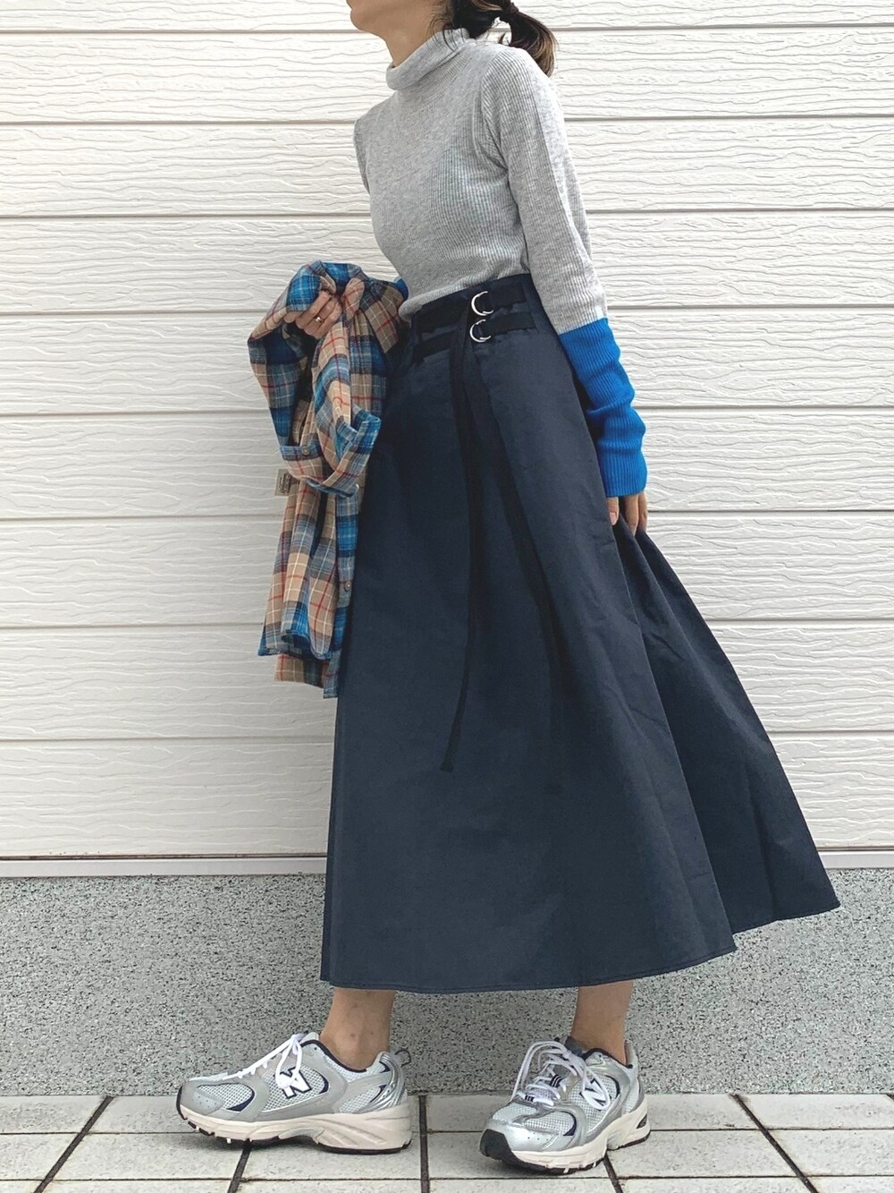 ブルー系のスカート、グレー系のニット/セーター、シルバー系のスニーカーを着用したレディースの冬コーディネートの2枚目の写真