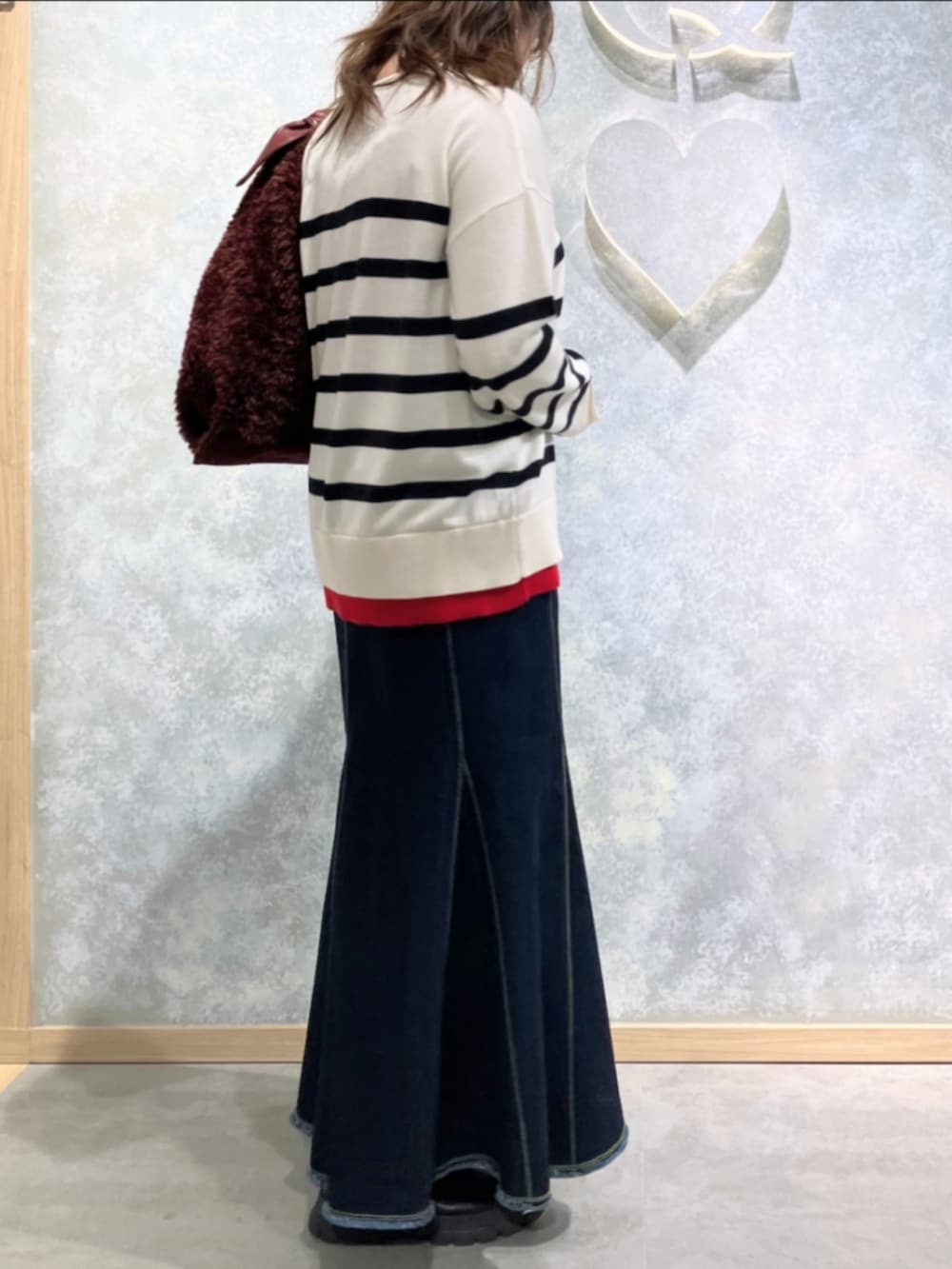 ブルー系のデニムスカート、レッド系のトートバッグ、ホワイト系のニット/セーターを着用したレディースの冬コーディネートの2枚目の写真