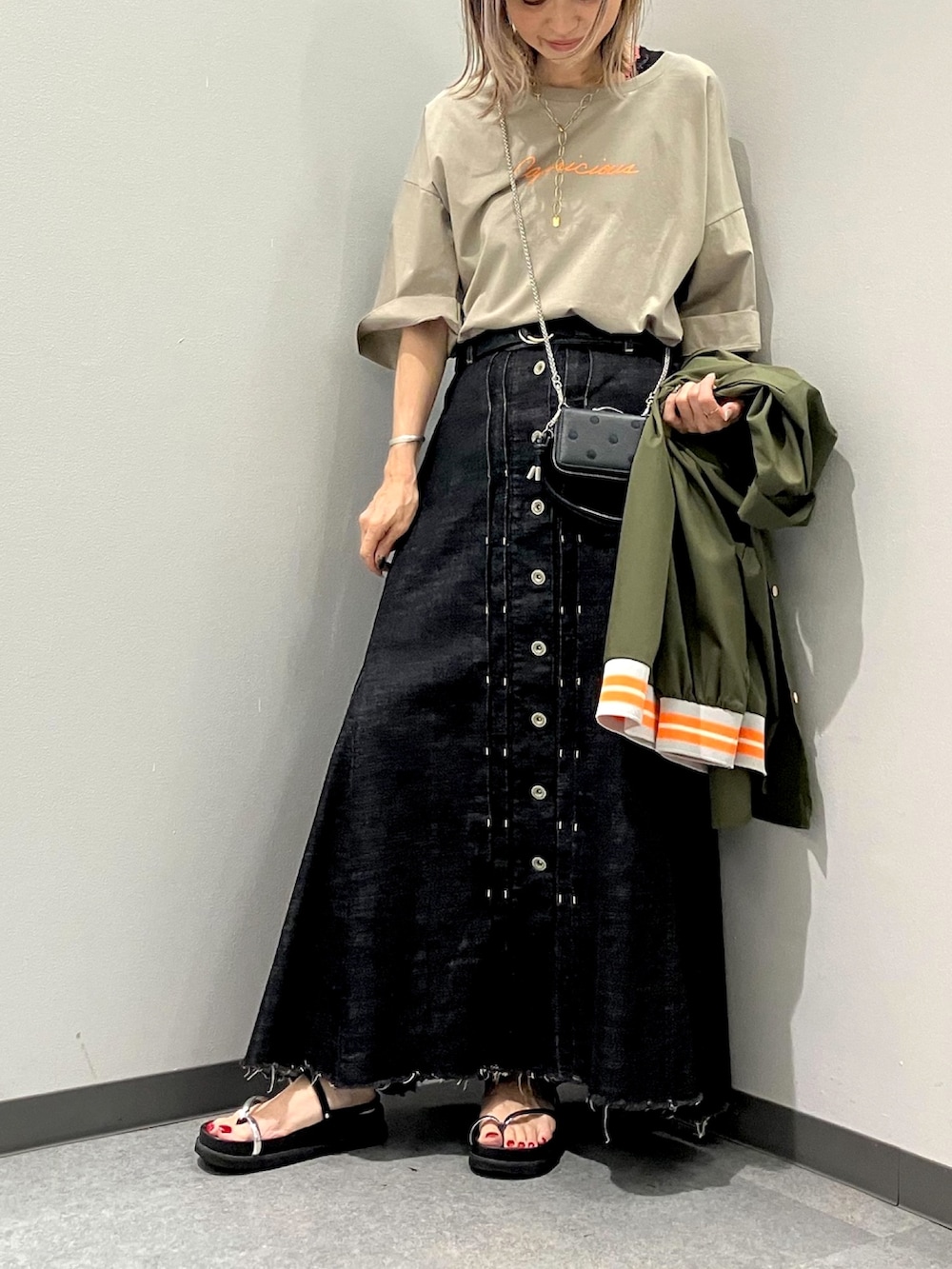 ブラック系のデニムスカート、ベージュ系のTシャツ/カットソー、ブラック系のサンダルを着用したレディースの夏コーディネートの3枚目の写真