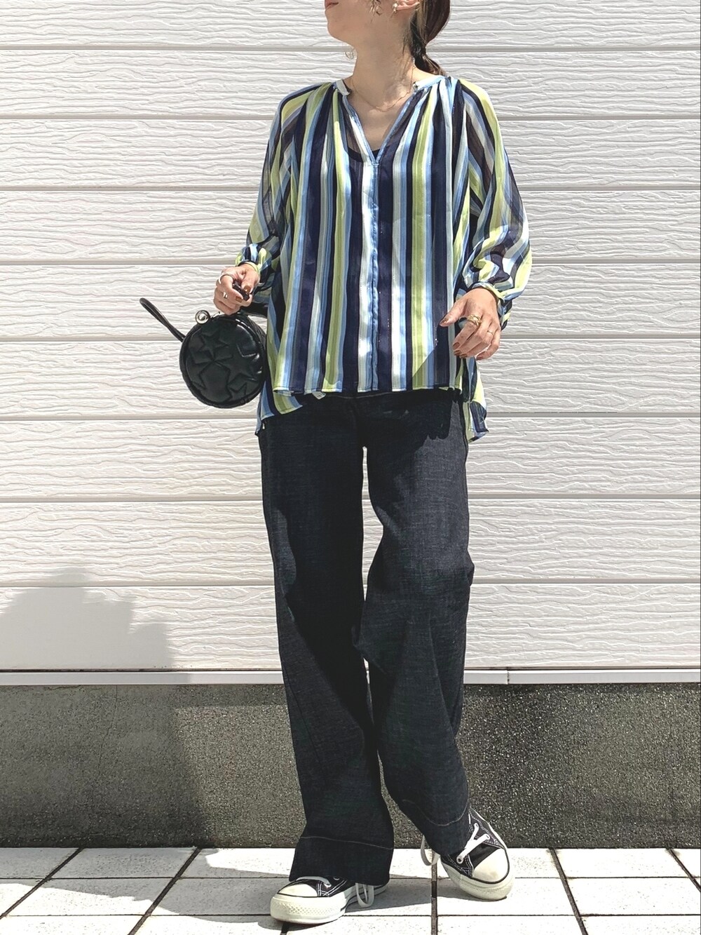 ブラック系のスニーカー、ブラック系のドラムバッグ、ブルー系のデニムパンツを着用したレディースの秋コーディネートの2枚目の写真