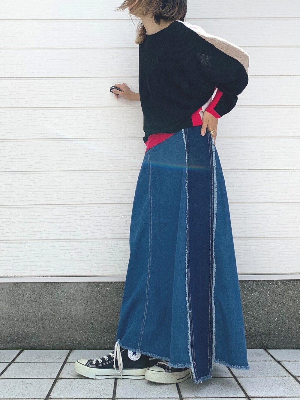 ブルー系のデニムスカート、ブラック系のスニーカー、ブラック系のニット/セーターを着用したレディースの夏コーディネートの2枚目の写真