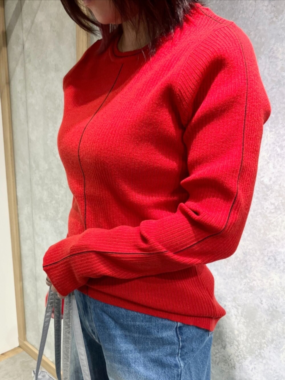 シルバー系のトートバッグ、ブルー系のデニムパンツ、レッド系のニット/セーターを着用したレディースの秋コーディネートの5枚目の写真