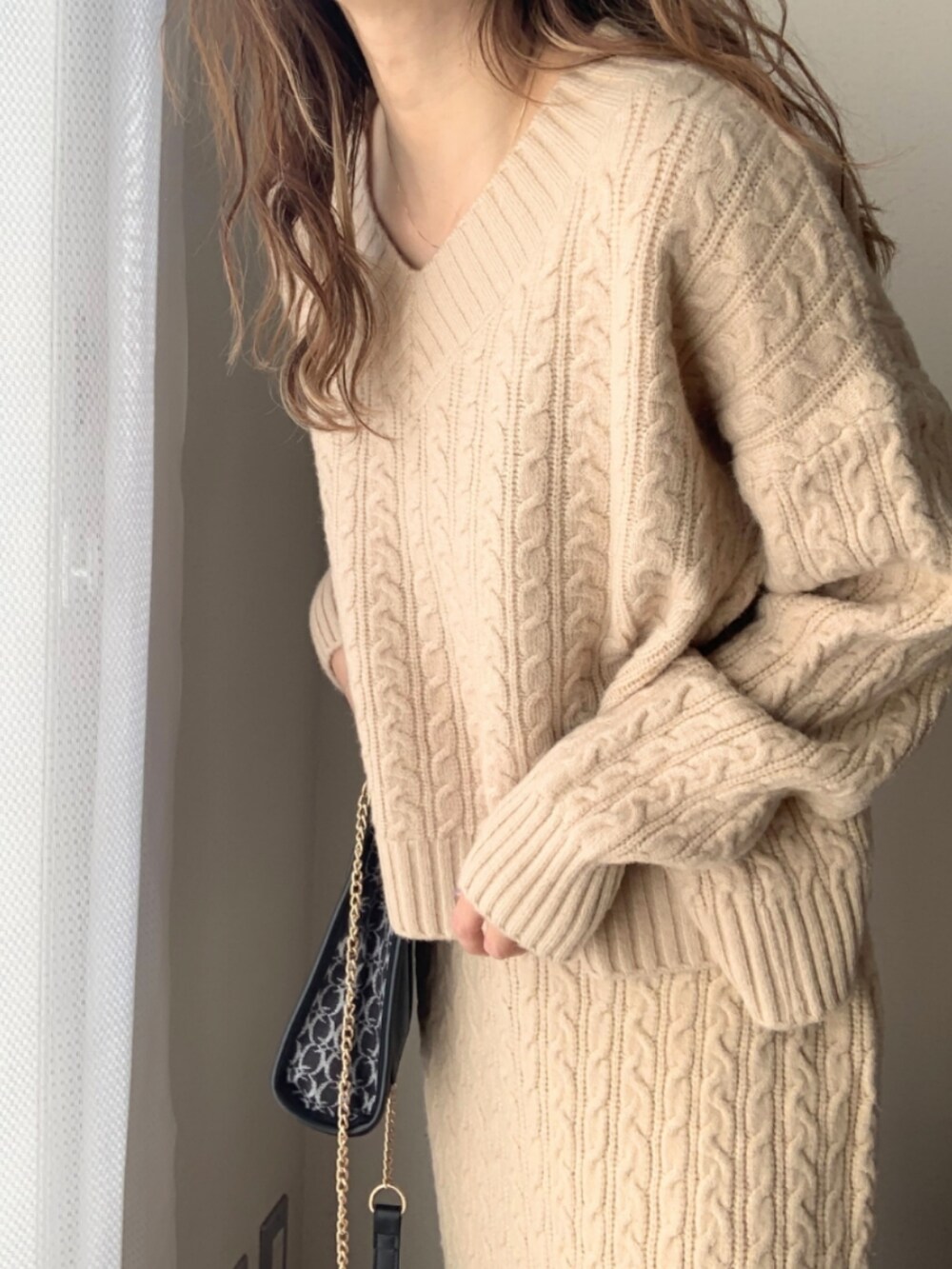 ブラック系のショルダーバッグ、ホワイト系のスニーカー、ベージュ系のニット/セーターを着用したレディースの冬コーディネートの5枚目の写真