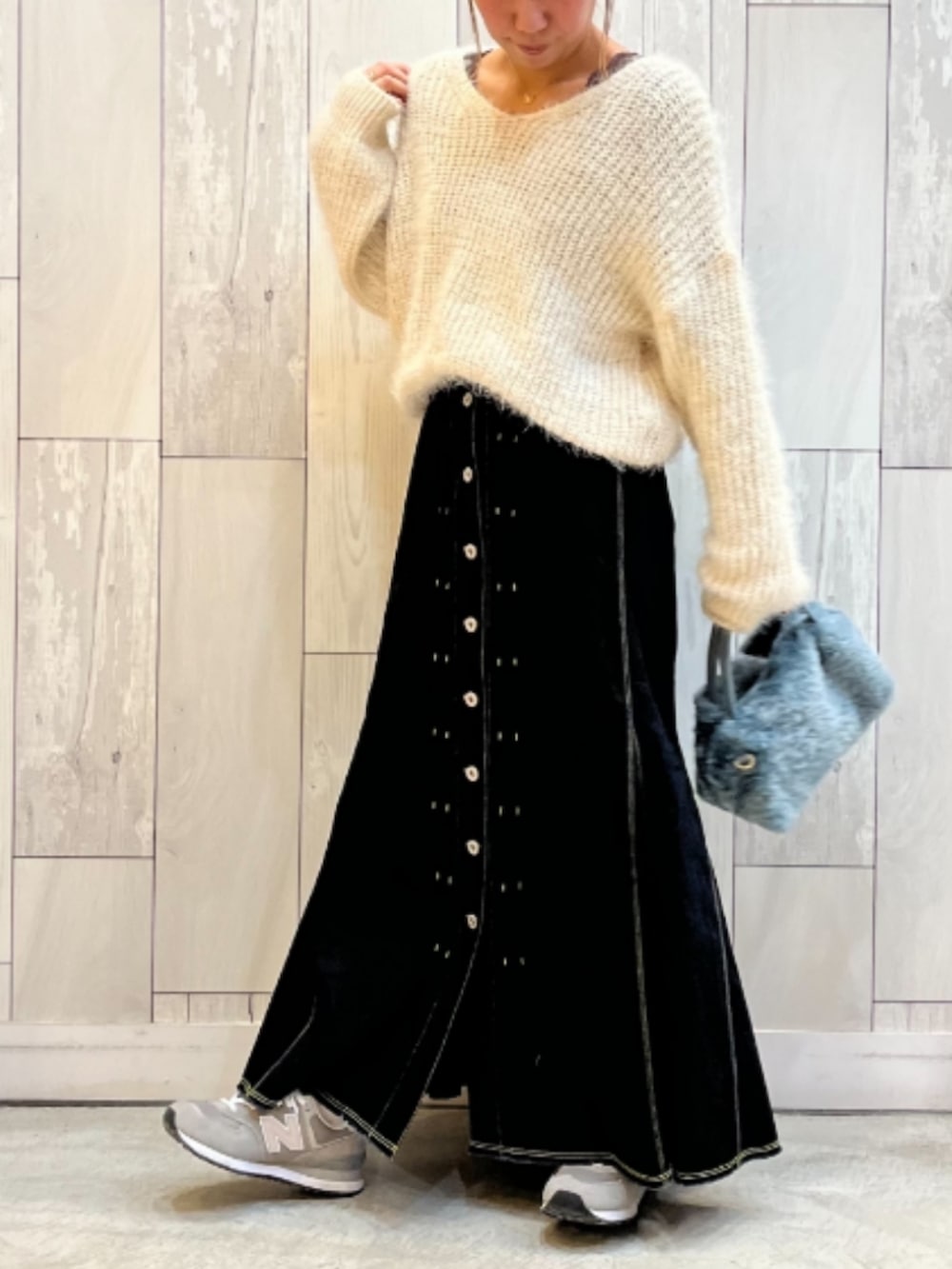 ブルー系のトートバッグ、ブラック系のデニムスカート、ホワイト系のニット/セーターを着用したレディースの冬コーディネートの2枚目の写真