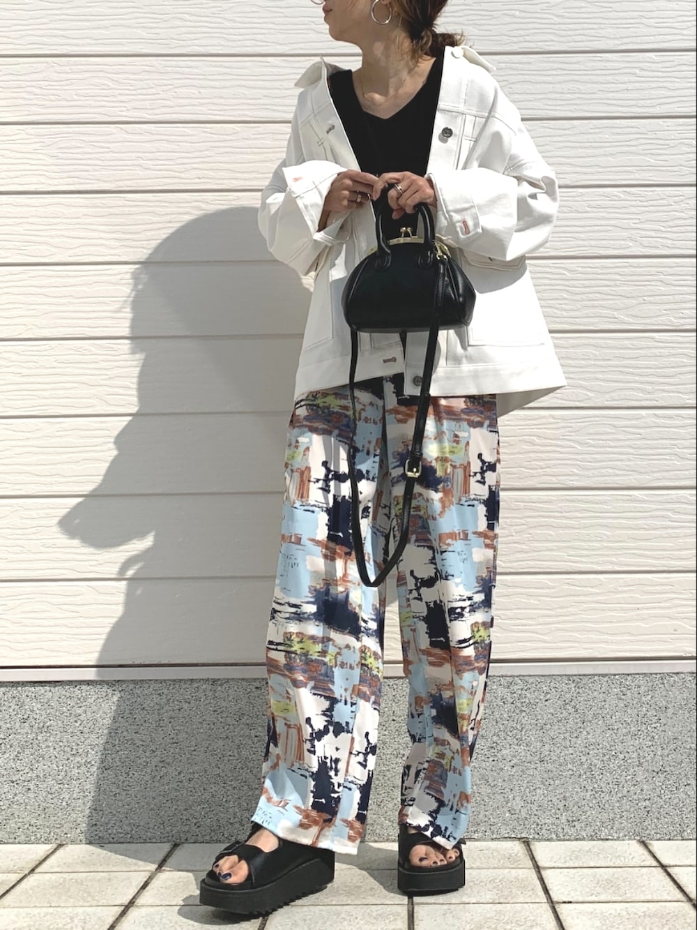 ブラック系のニット/セーター、ホワイト系のデニムジャケット、ブラック系のサンダルを着用したレディースの春コーディネートの2枚目の写真