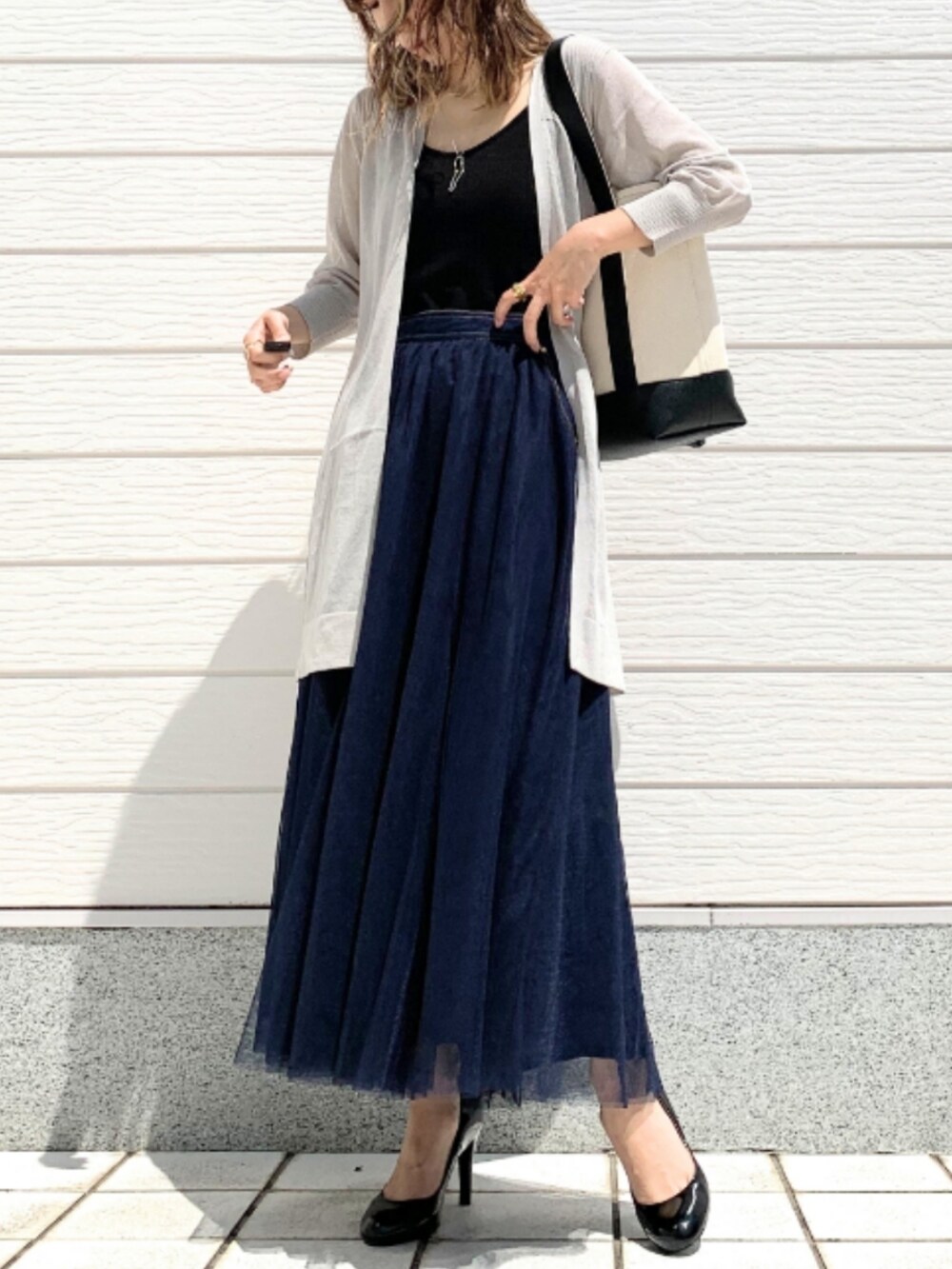 ブラック系のハンドバッグ、ブルー系のスカート、グレー系のカーディガン/ボレロを着用したレディースの春コーディネートの2枚目の写真