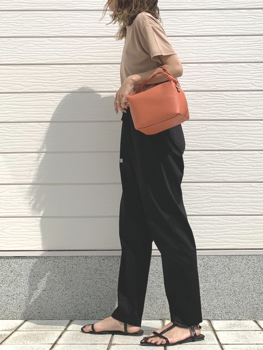 ブラック系のその他パンツ、ベージュ系のTシャツ/カットソー、オレンジ系のハンドバッグを着用したレディースの春コーディネートの2枚目の写真