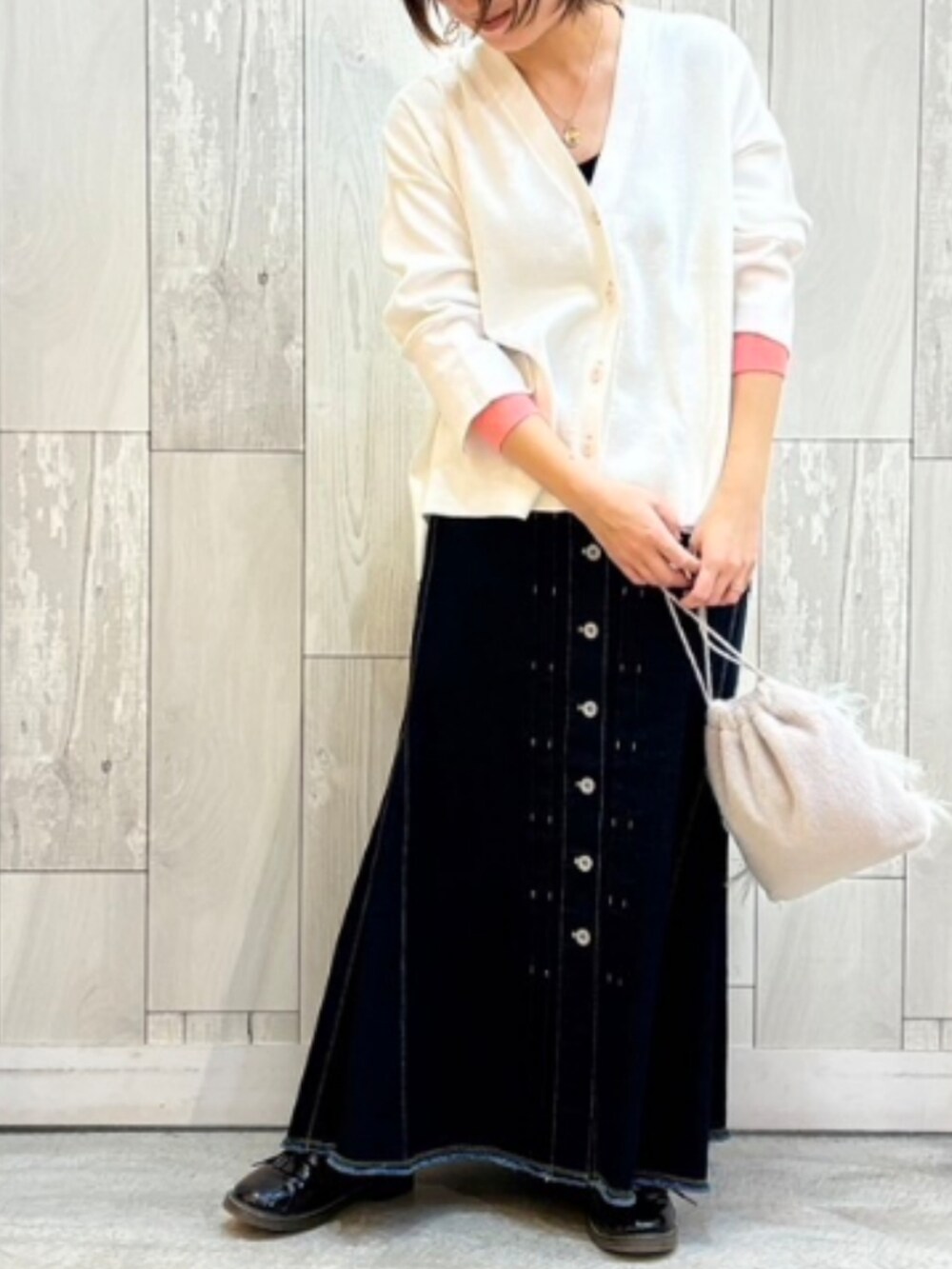 グレー系のクラッチバッグ、ブラック系のデニムスカート、ホワイト系のカーディガン/ボレロを着用したレディースの冬コーディネートの2枚目の写真