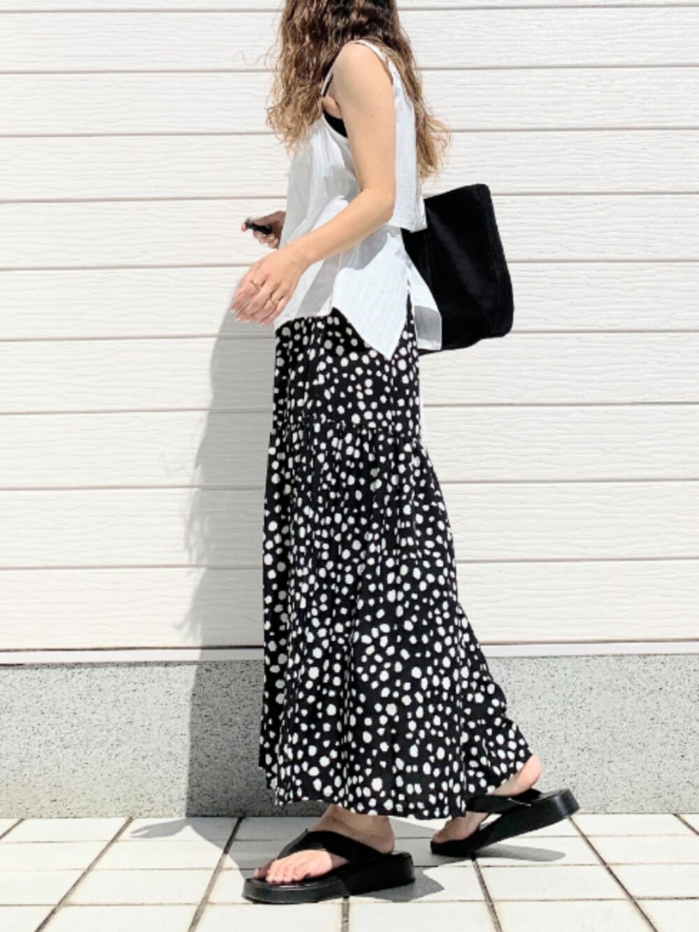 ブラック系のスカート、ホワイト系のトートバッグ、ホワイト系のシャツ/ブラウスを着用したレディースの夏コーディネートの2枚目の写真