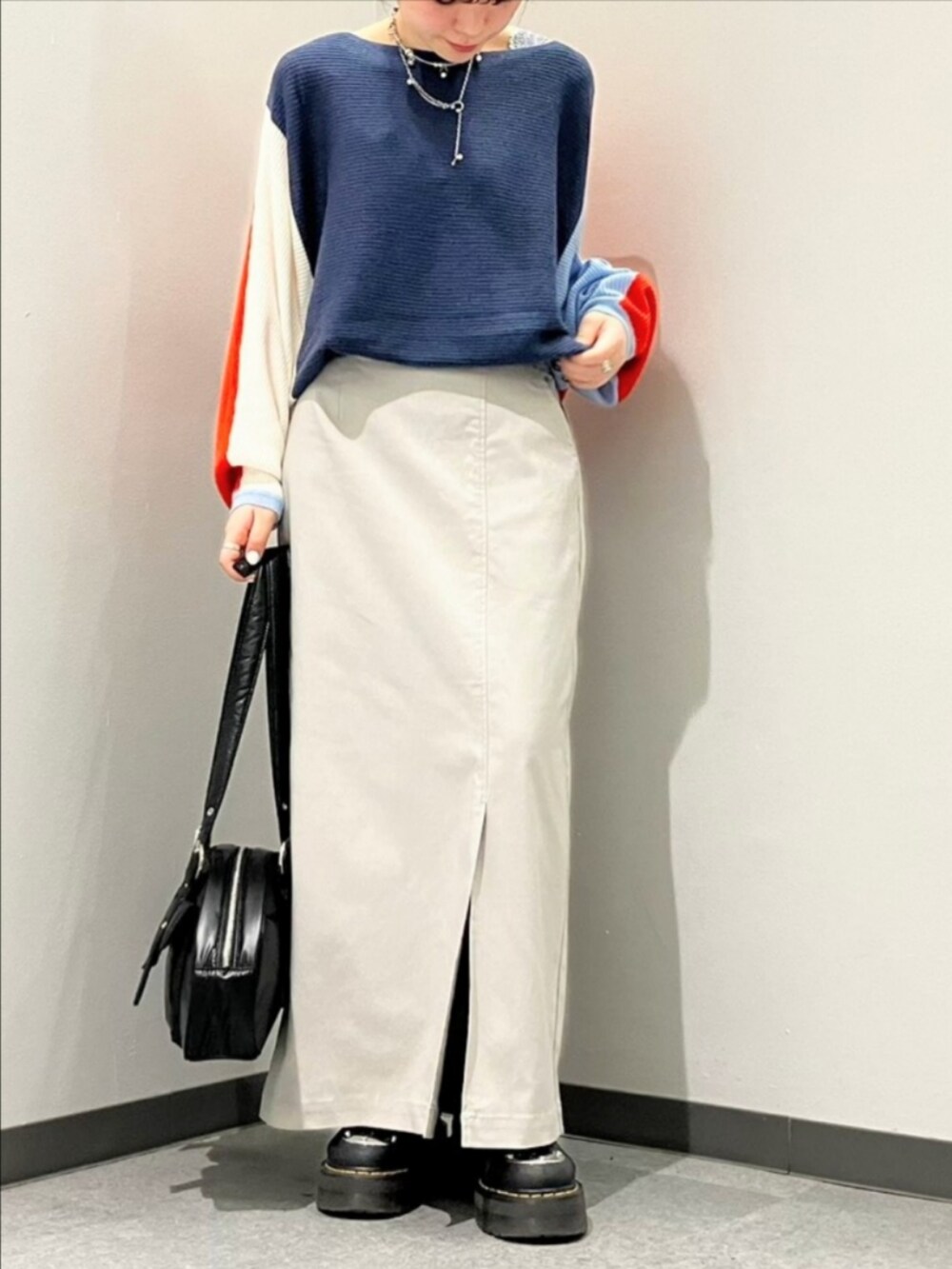 オレンジ系のニット/セーター、グレー系のスカート、ブラック系のボストンバッグを着用したレディースの秋コーディネートの2枚目の写真