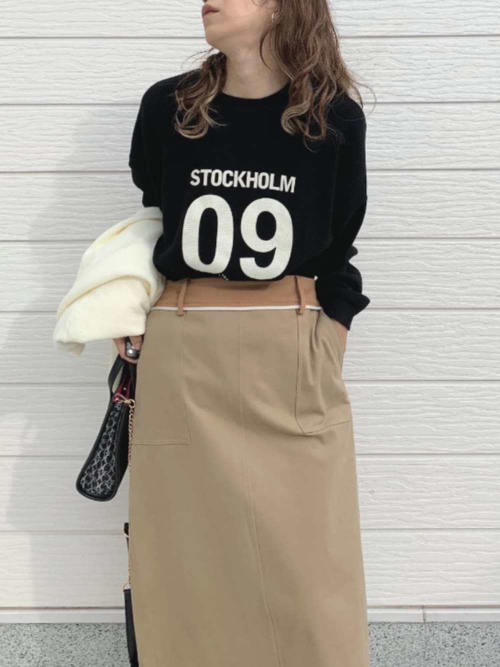 ブラック系のショルダーバッグ、ベージュ系のスカート、ブラック系のTシャツ/カットソーを着用したレディースの秋コーディネートの4枚目の写真