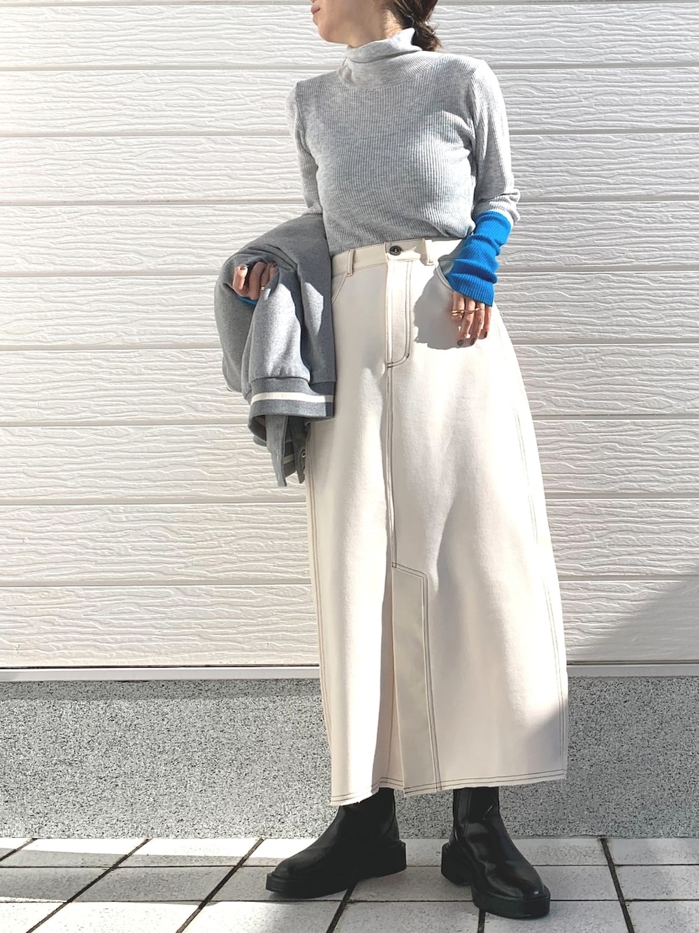 グレー系のスタジャン、ホワイト系のスカート、グレー系のニット/セーターを着用したレディースの秋コーディネートの3枚目の写真
