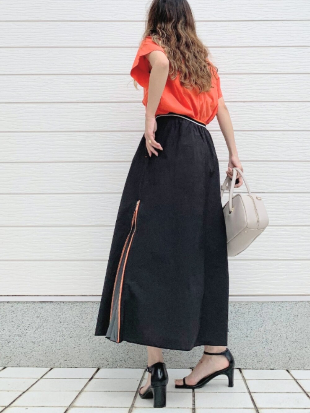 ブラック系のスカート、ホワイト系のボストンバッグ、オレンジ系のTシャツ/カットソーを着用したレディースの夏コーディネートの3枚目の写真