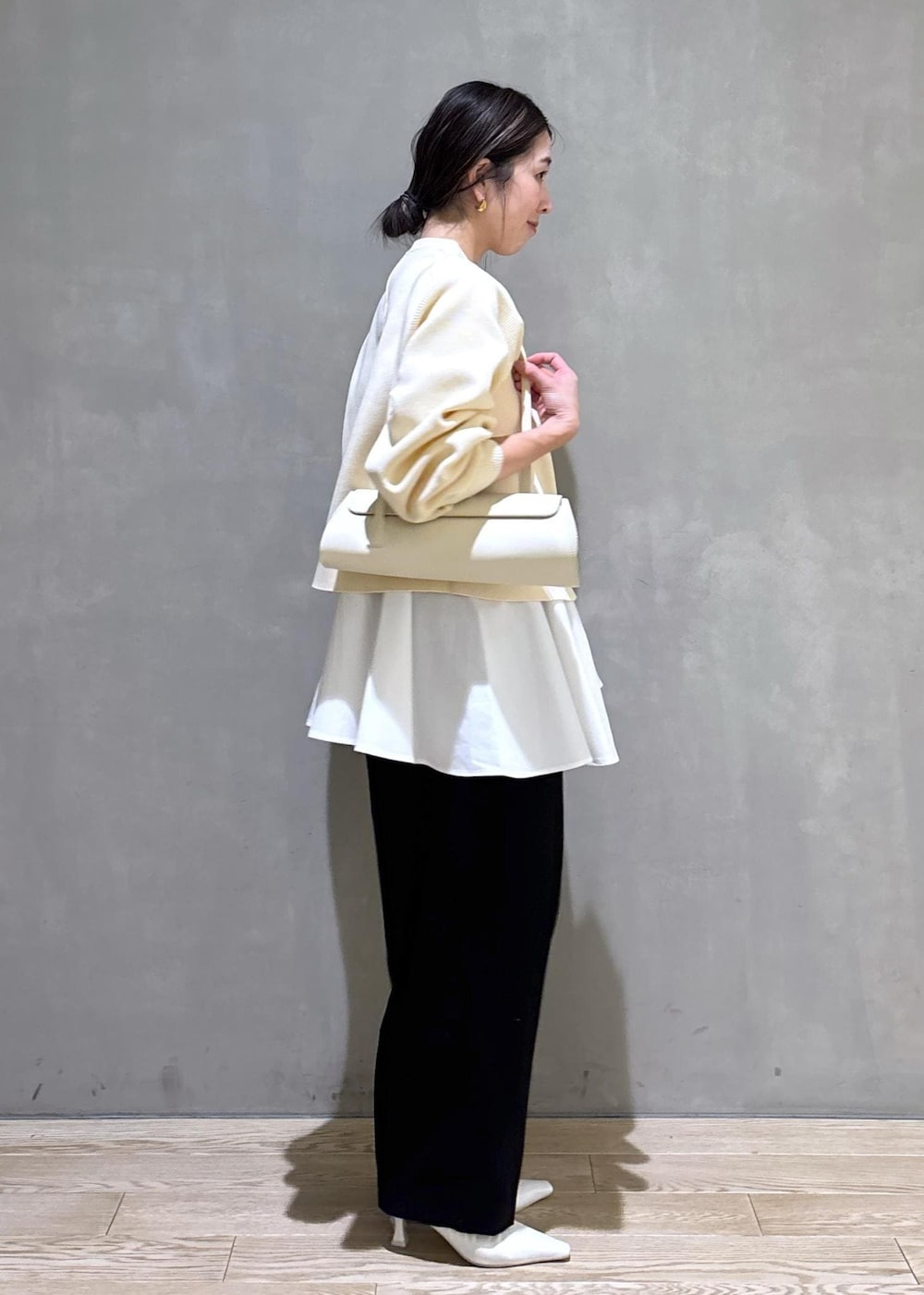 ホワイト系のパンプス、ブラック系のスラックス、ホワイト系のショルダーバッグを着用したレディースの冬コーディネートの3枚目の写真