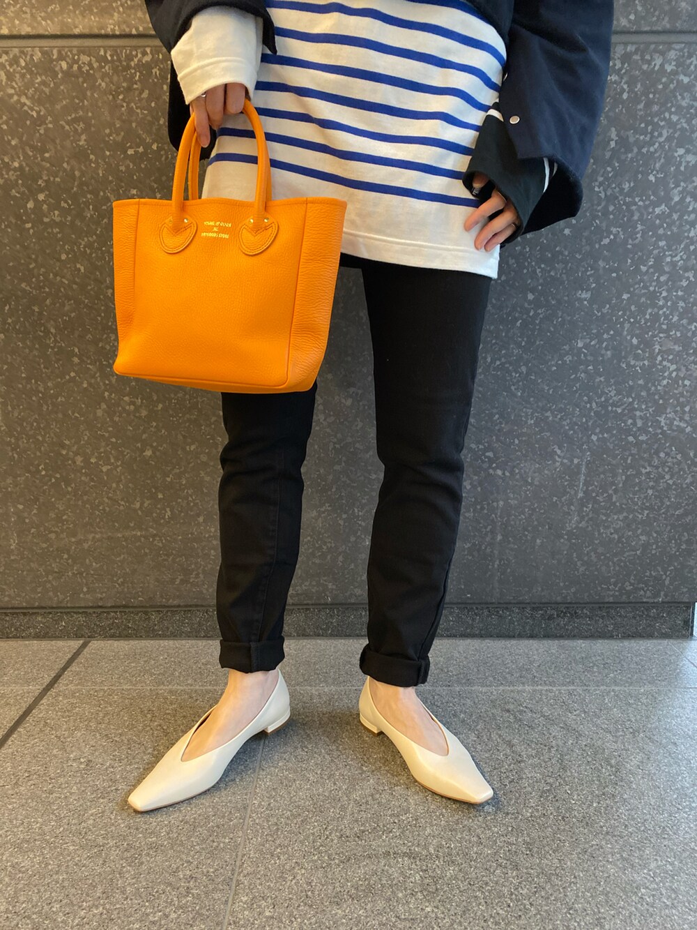 ブラック系のデニムパンツ、オレンジ系のトートバッグ、ブルー系のスウェットを着用したレディースの春コーディネートの3枚目の写真