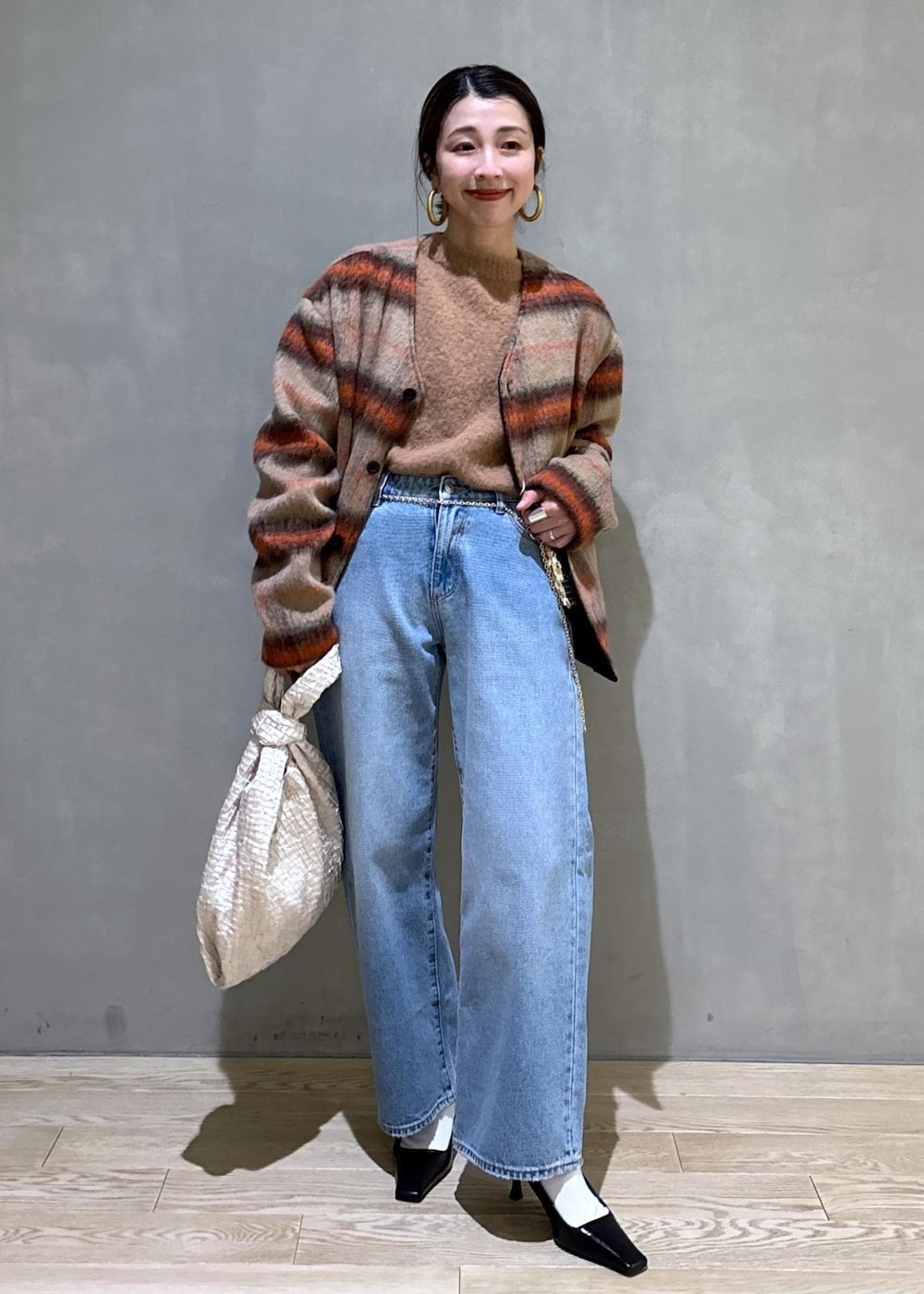 ホワイト系のハンドバッグ、ゴールド系のショルダーバッグ、ブルー系のデニムパンツを着用したレディースの冬コーディネートの2枚目の写真