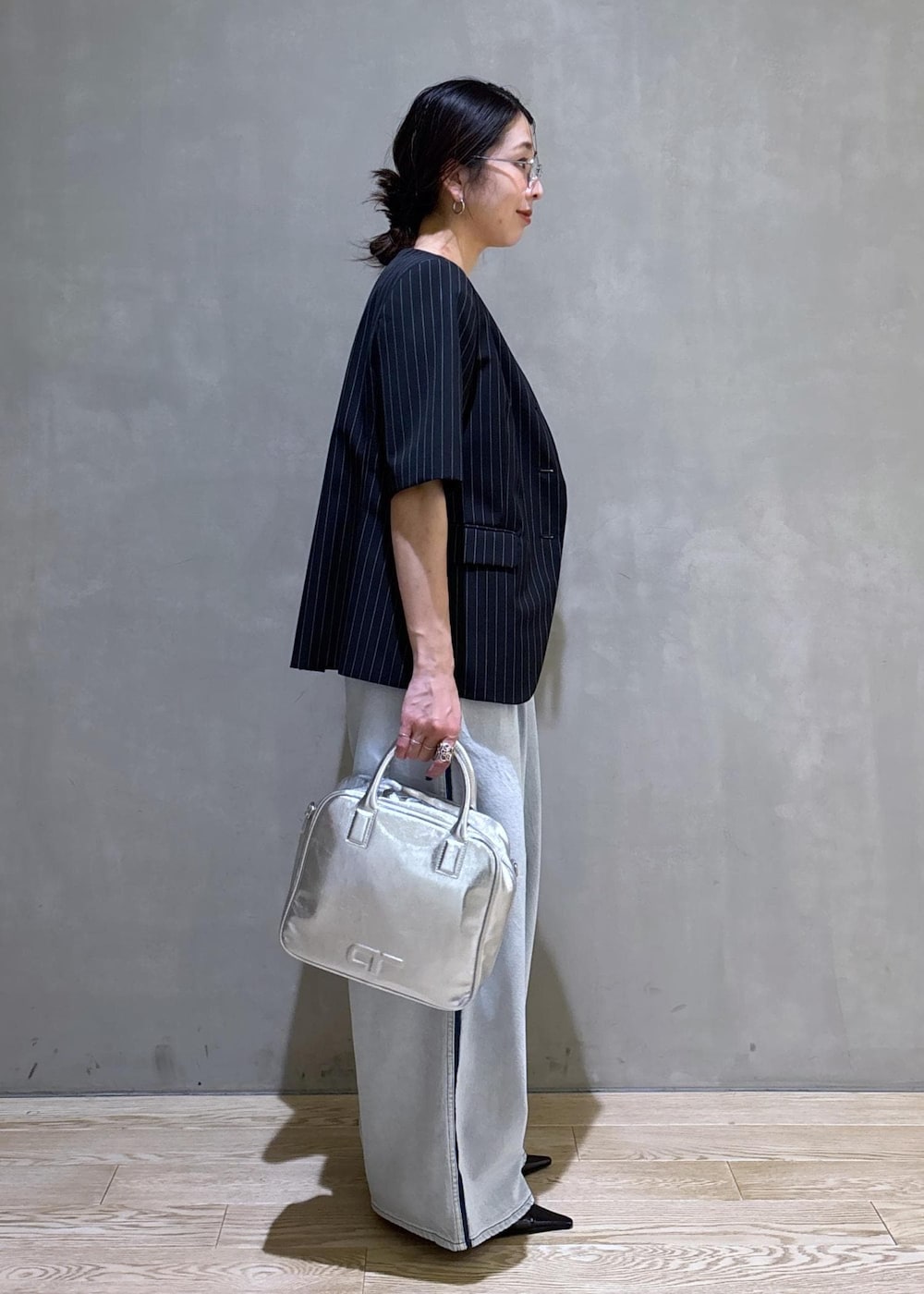 ブルー系のデニムパンツ、ブラック系のノーカラージャケット、シルバー系のボストンバッグを着用したレディースの春コーディネートの6枚目の写真