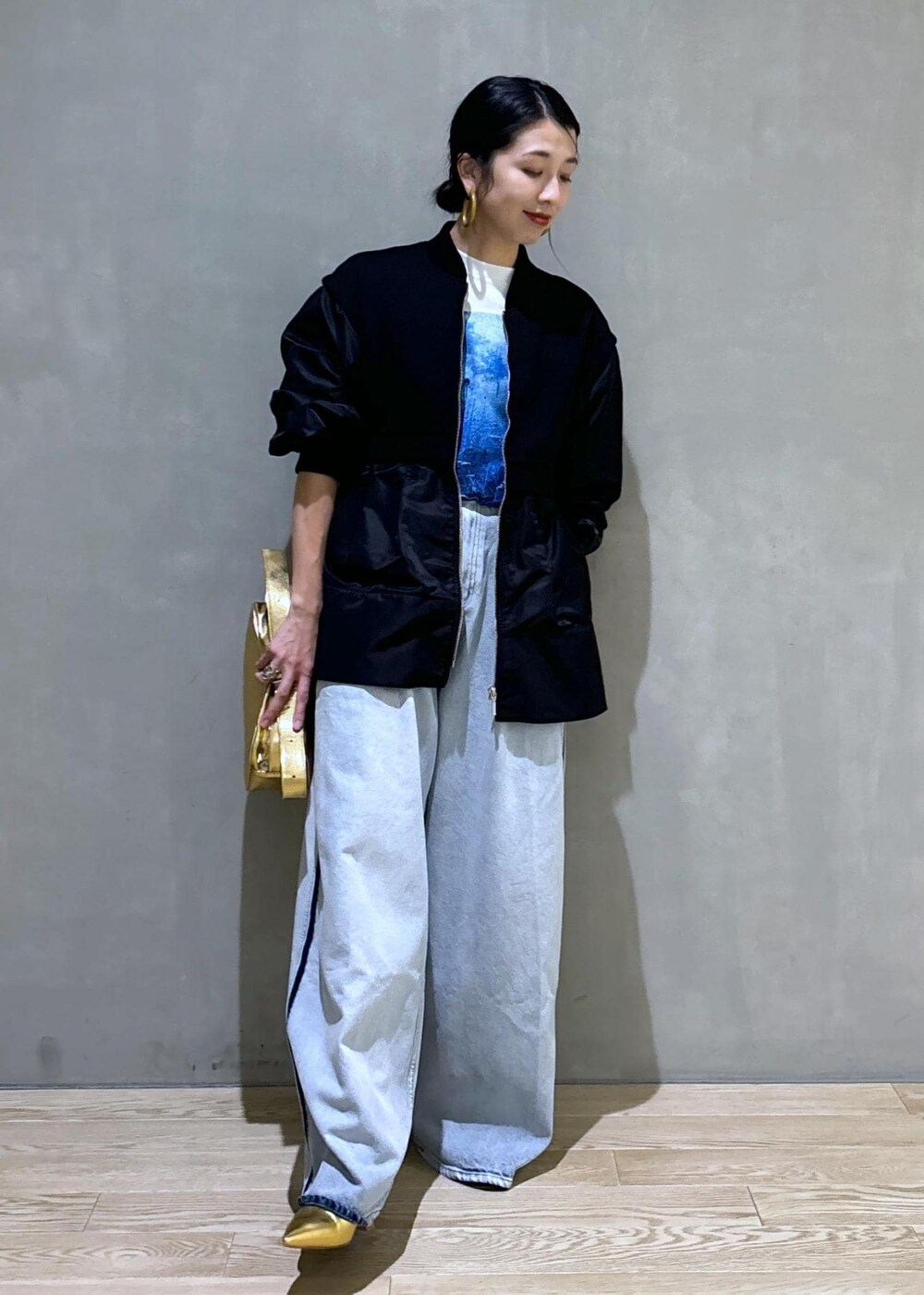 ゴールド系のショルダーバッグ、ブラック系のブルゾン、ホワイト系のTシャツ/カットソーを着用したレディースの秋コーディネートの4枚目の写真