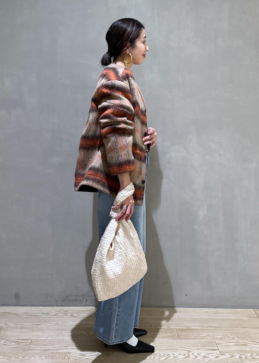 ホワイト系のハンドバッグ、ゴールド系のショルダーバッグ、ブルー系のデニムパンツを着用したレディースの冬コーディネートの3枚目の写真