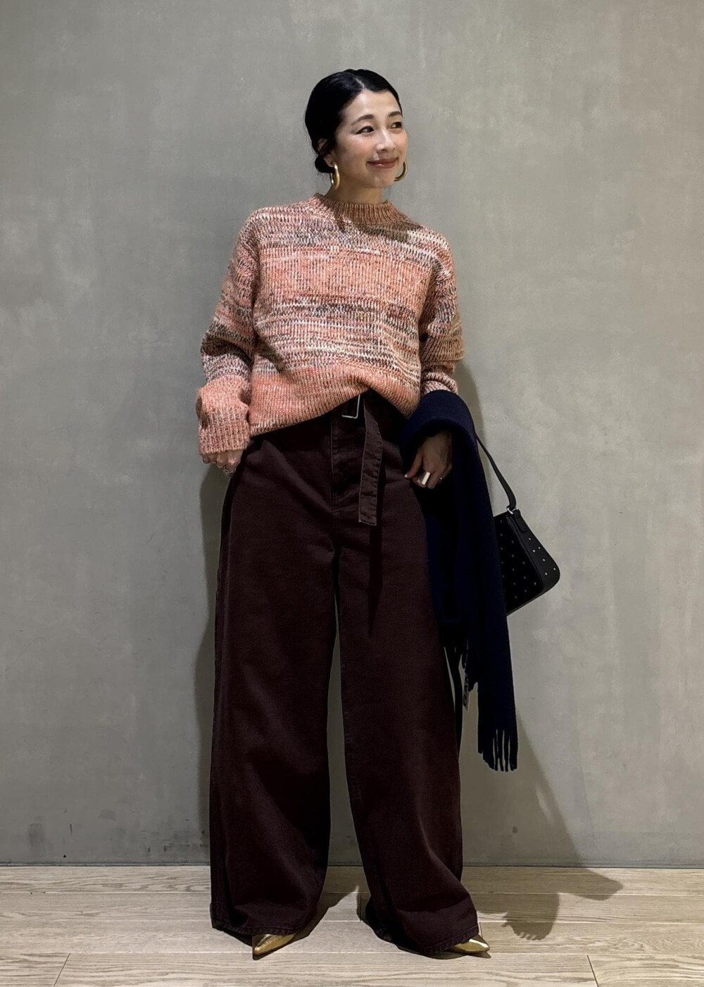 オレンジ系のニット/セーター、ブラック系のショルダーバッグ、ブラウン系のその他パンツを着用したレディースの秋コーディネートの2枚目の写真