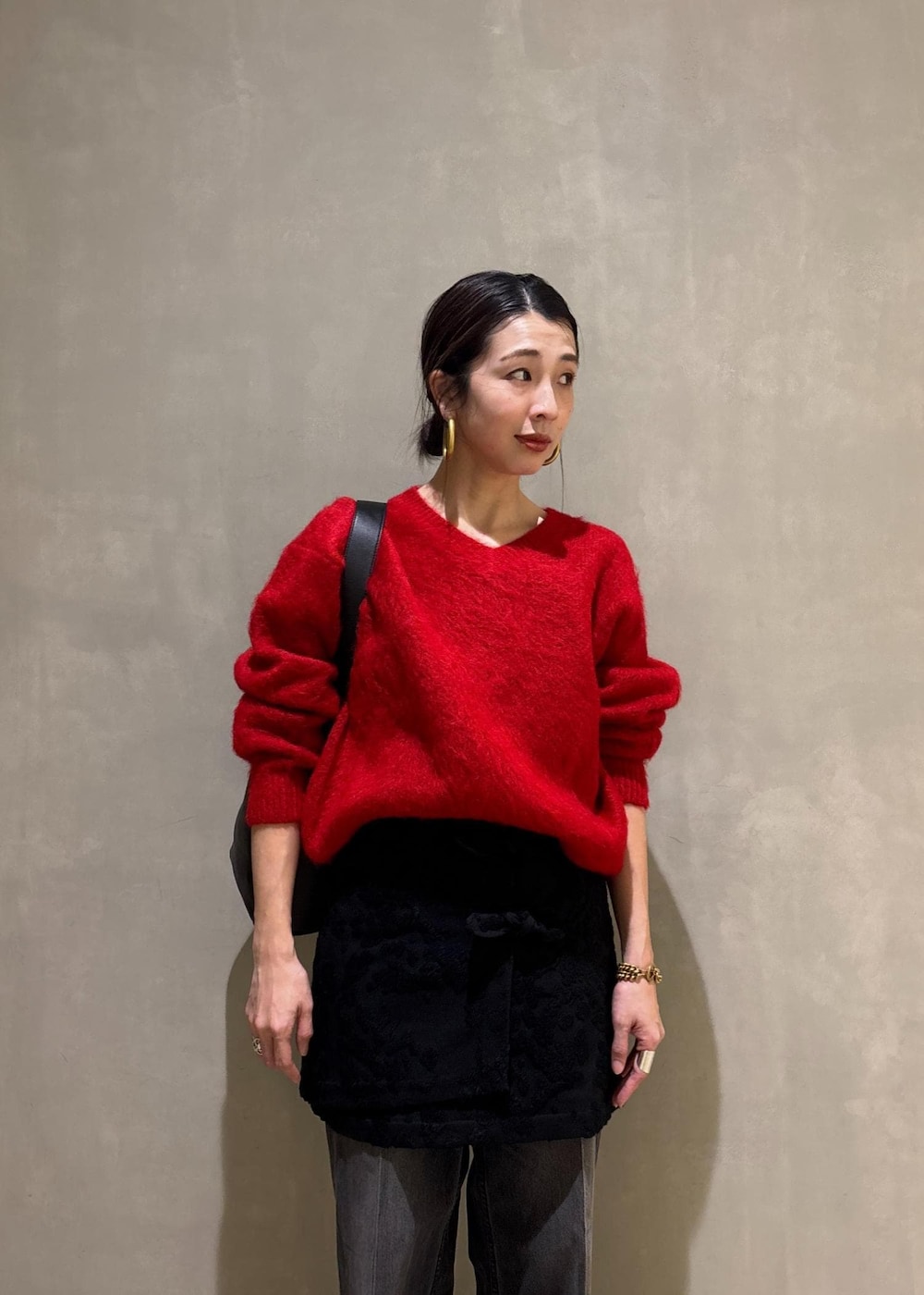 レッド系のニット/セーター、ブラック系のスカート、ブラック系のデニムパンツを着用したレディースの冬コーディネートの9枚目の写真