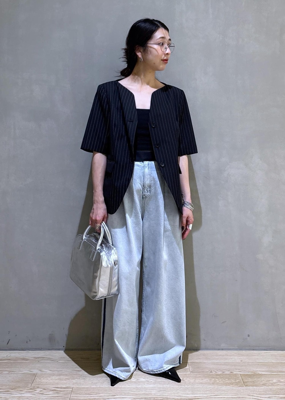 ブルー系のデニムパンツ、ブラック系のノーカラージャケット、シルバー系のボストンバッグを着用したレディースの春コーディネートの4枚目の写真