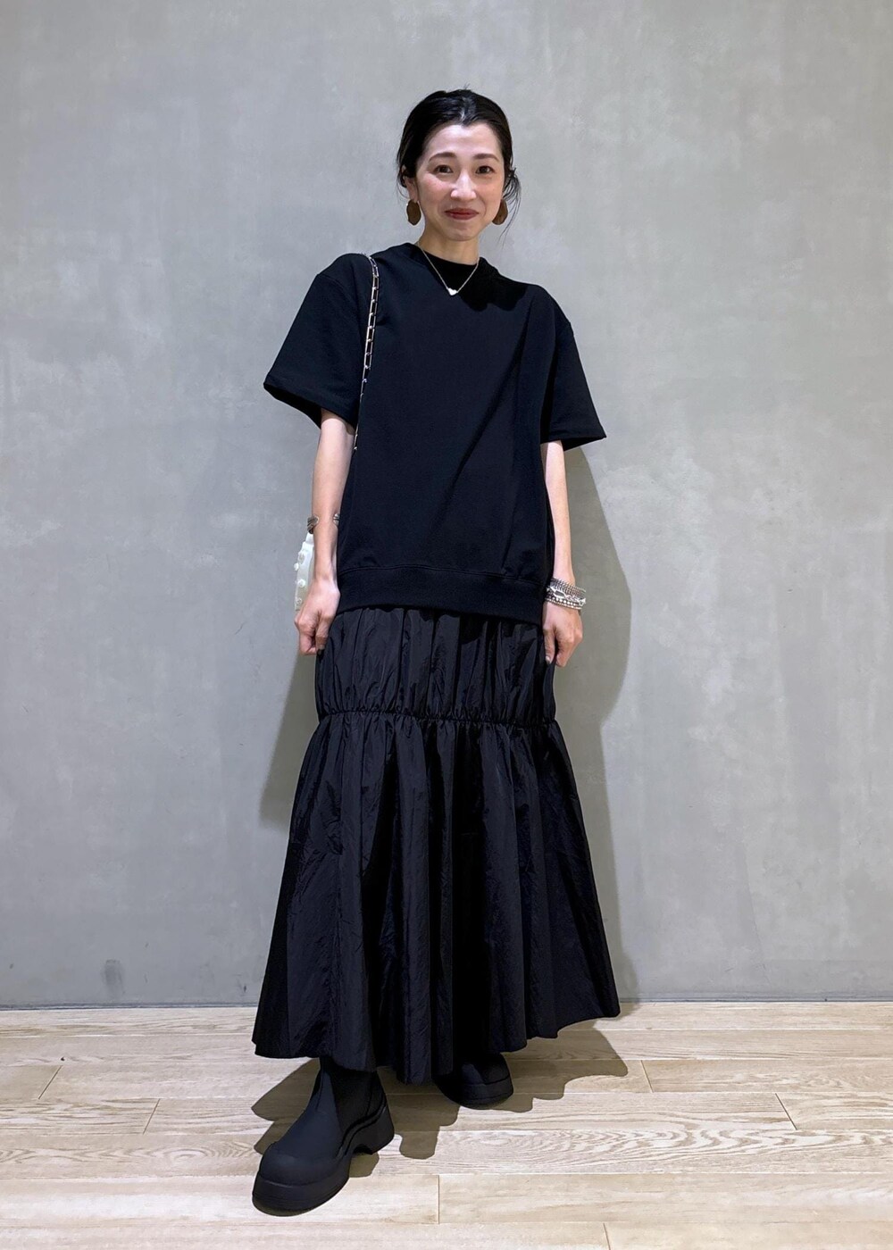 ホワイト系のショルダーバッグ、ブラック系のブーツ、ブラック系のワンピースを着用したレディースの夏コーディネートの2枚目の写真