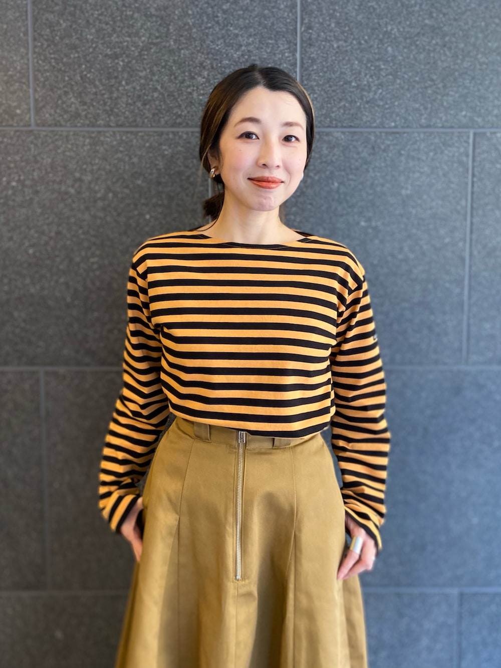 オレンジ系のTシャツ/カットソー、ブラウン系のスカート、ベージュ系のブーツを着用したレディースの春コーディネートの2枚目の写真