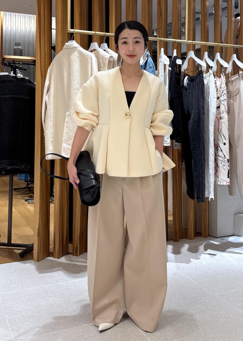 ブラック系のショルダーバッグ、ホワイト系のパンプス、ベージュ系のスラックスを着用したレディースの冬コーディネートの2枚目の写真